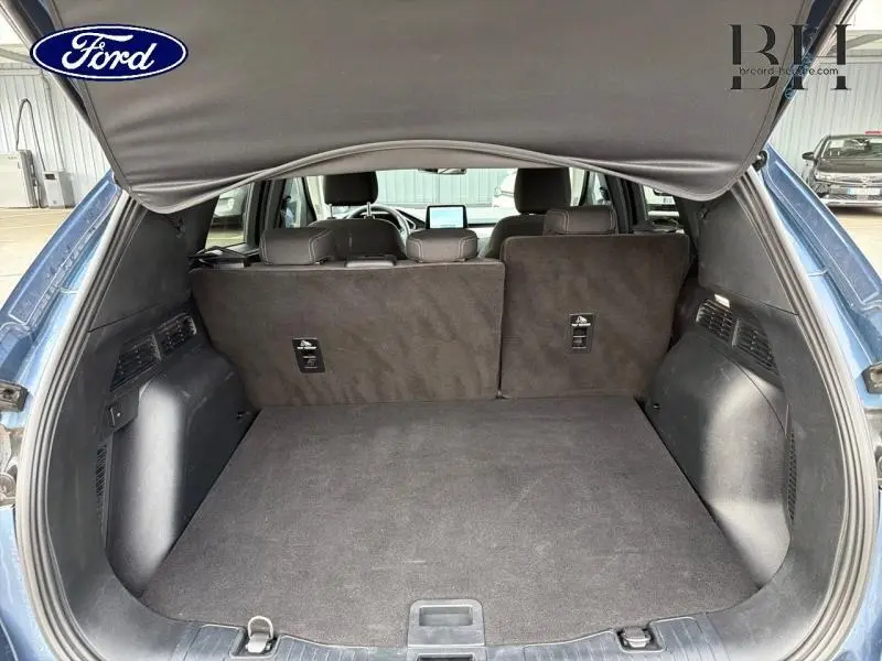 Coffre ouvert vu de l'arrière du Ford Kuga bleu azur métallisé, banquette arrière noire en tissu relevée.