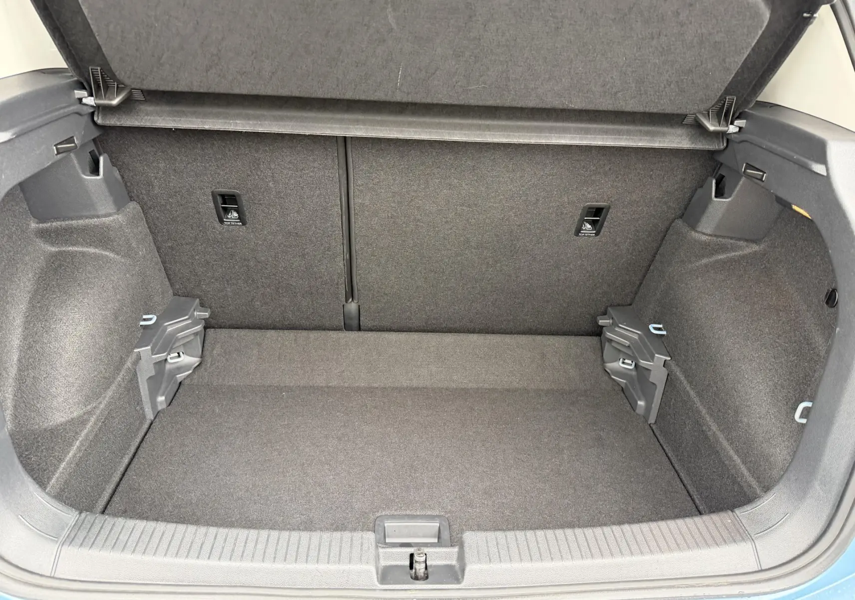 Coffre ouvert du Volkswagen T-Cross bleu, vue intérieure montrant l'espace de chargement et les fixations ISOFIX.