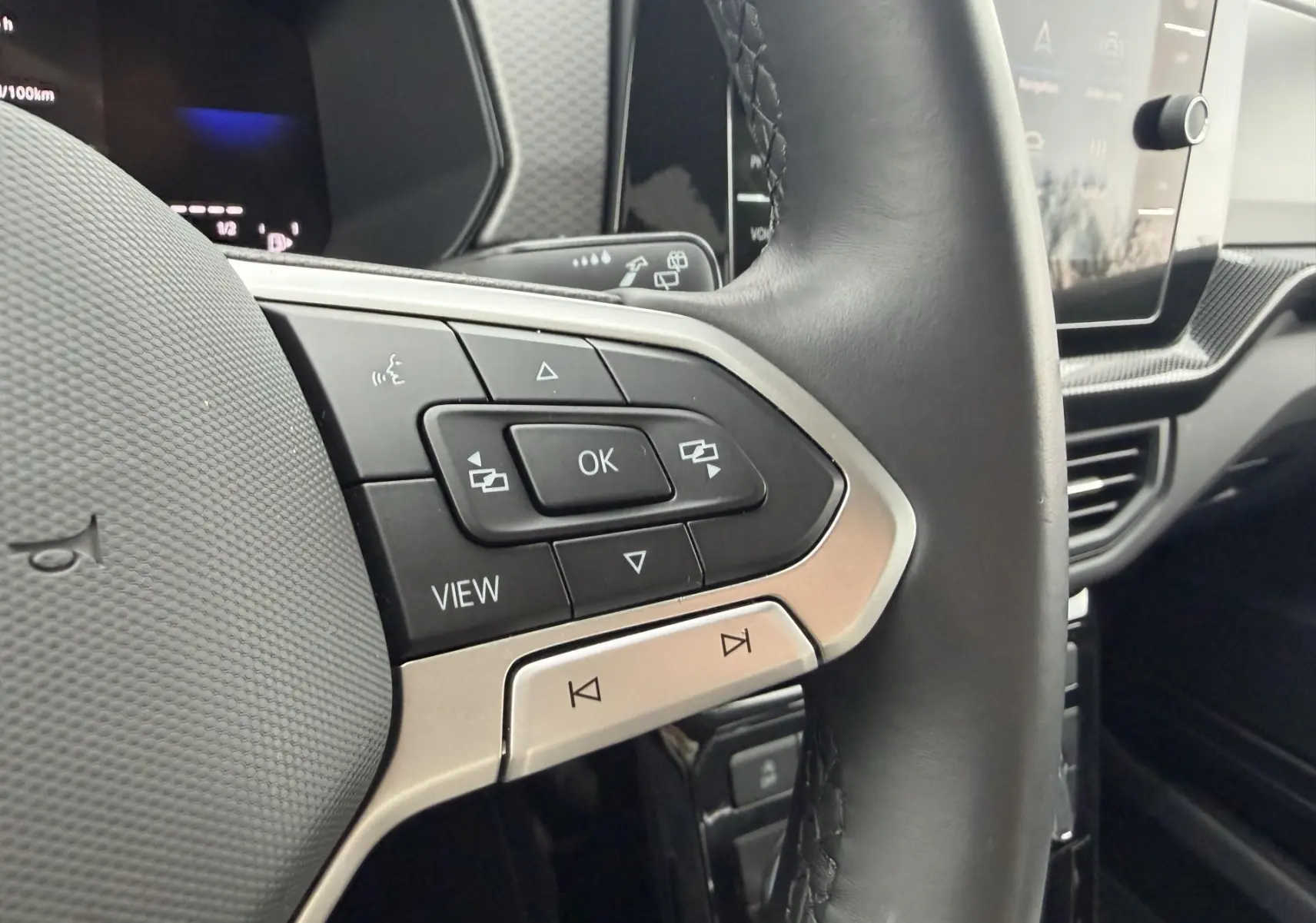 Gros plan sur le volant multifonction cuir noir du Volkswagen T-Cross 2025, avec commandes intégrées et écran tactile en arrière-plan.