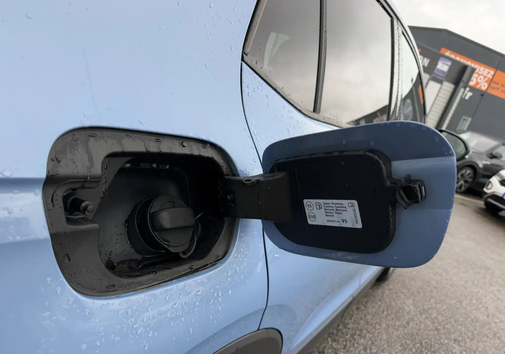 Gros plan sur la trappe à carburant bleue ouverte du Volkswagen T-Cross 2025, côté gauche, sous la pluie.
