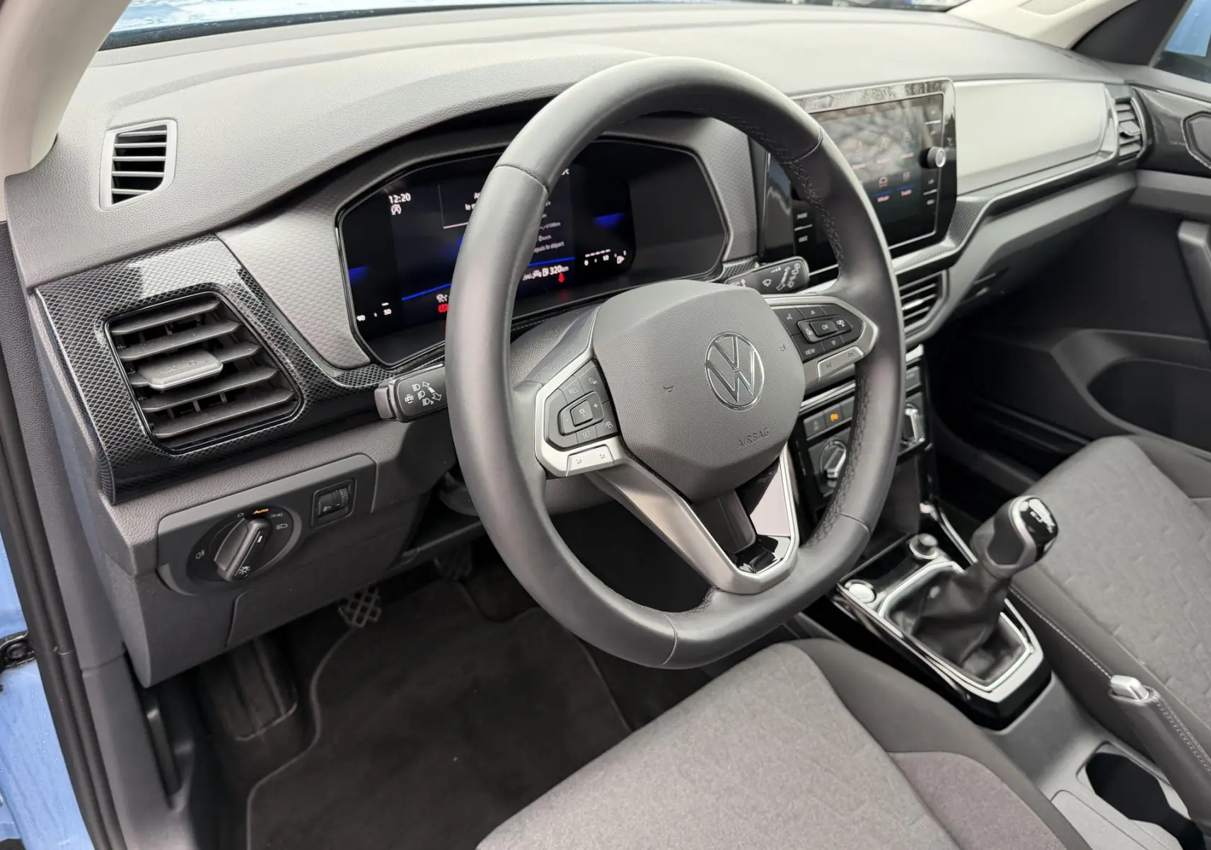 Vue intérieure côté conducteur du Volkswagen T-Cross bleu 2025, volant cuir multifonction et boîte manuelle visible.