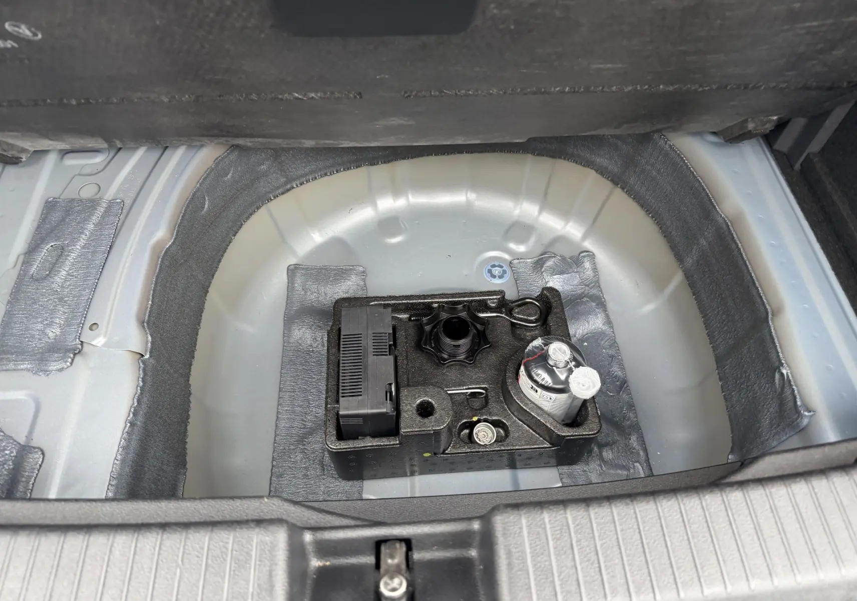 Vue plongeante sur le coffre ouvert d'un Volkswagen T-Cross 2025, montrant le rangement sous plancher avec kit de réparation pneus.