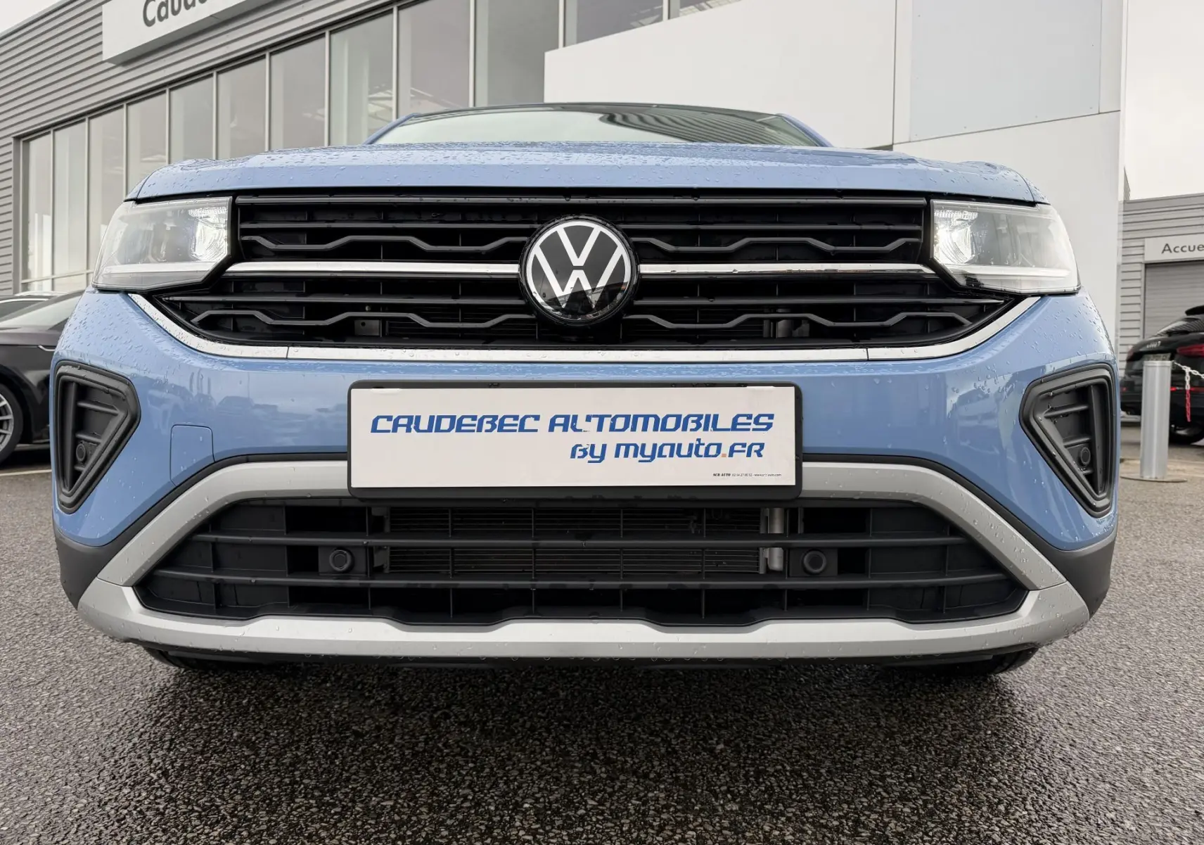 Vue frontale rapprochée du Volkswagen T-Cross bleu 2025 avec calandre noire et logo VW central bien visible.