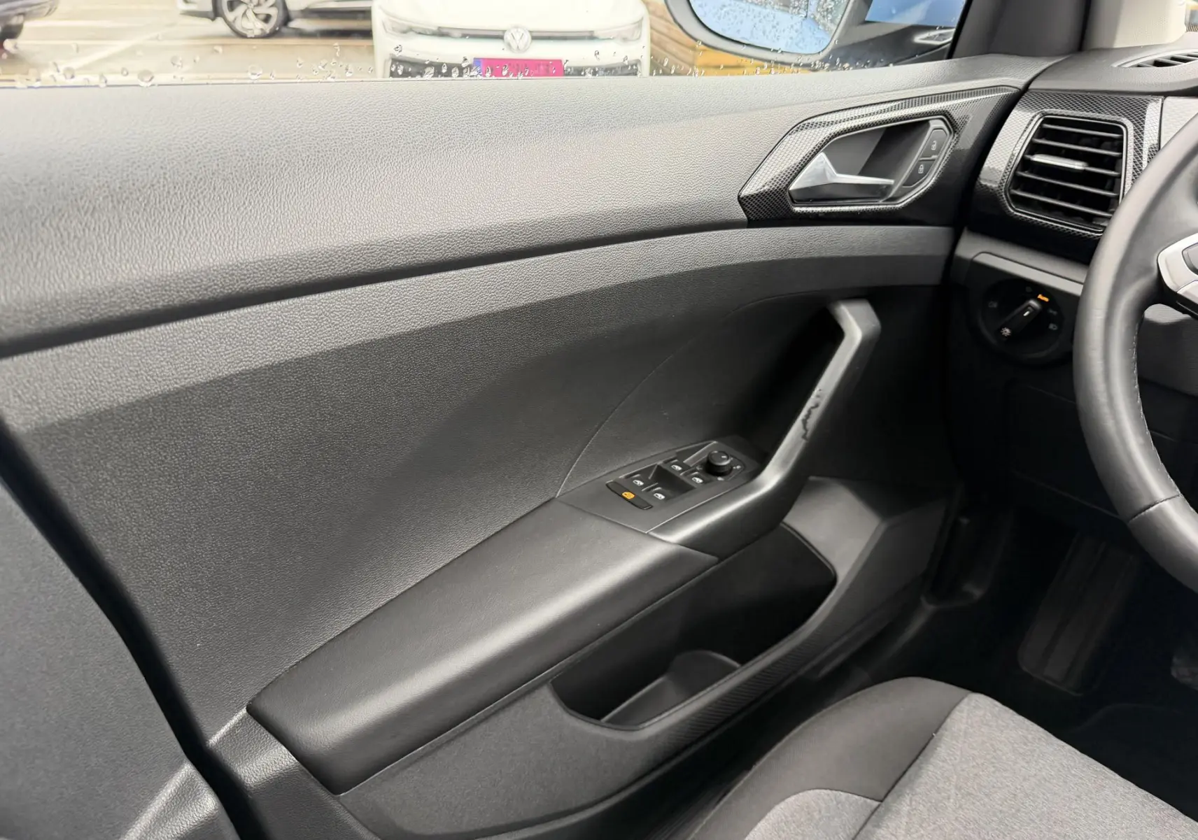 Vue intérieure côté conducteur du Volkswagen T-Cross 2025, montrant la portière noire avec commandes des vitres et rétroviseurs.