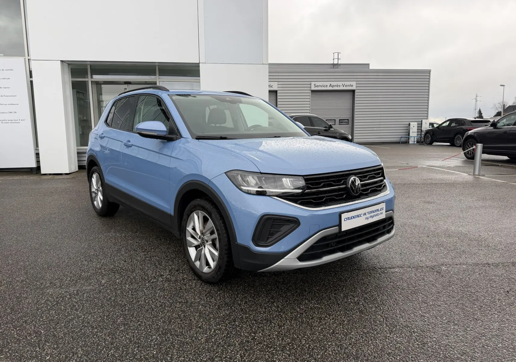 Volkswagen T-Cross bleu en 3/4 avant droit, avec jantes alliage et calandre noire brillante sous la pluie.