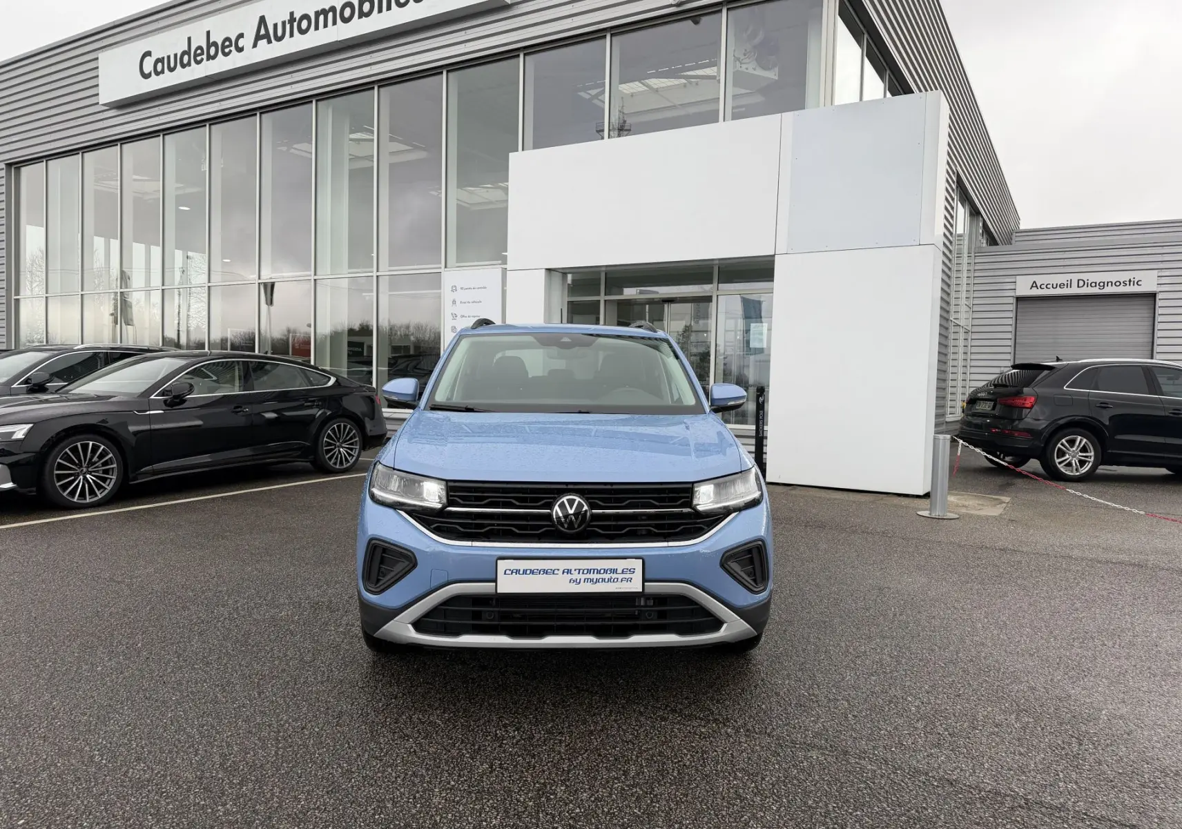 Vue avant d'un Volkswagen T-Cross bleu 2025 garé devant un concessionnaire avec calandre noire et détails argentés.