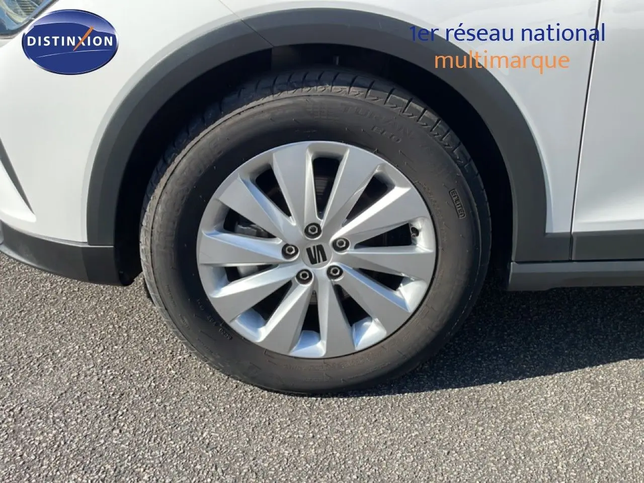 Gros plan sur la roue avant gauche d'une SEAT Arona blanc métal avec jante argentée, partie basse de la carrosserie visible.