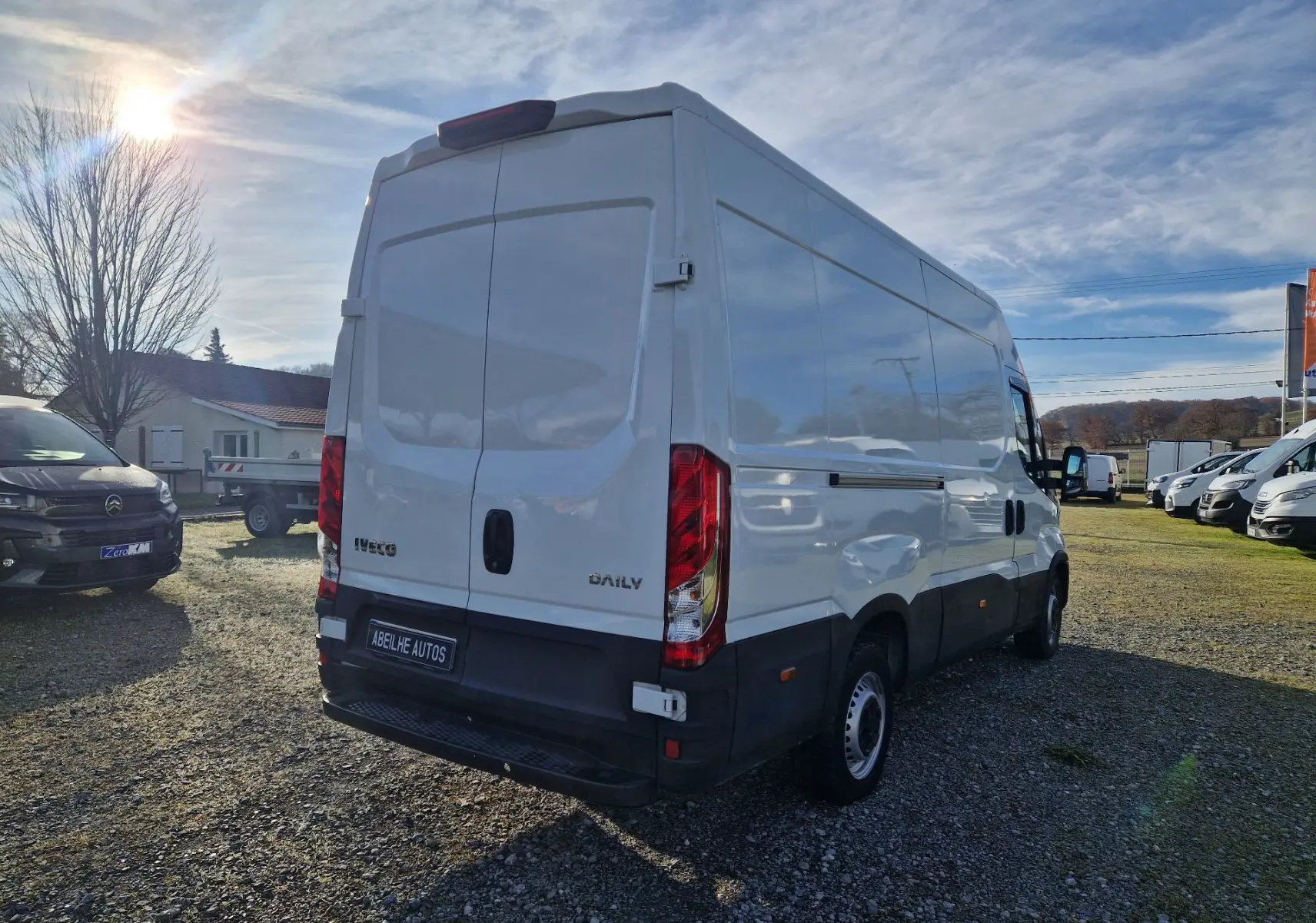 Vue 3/4 arrière droite d'un utilitaire Iveco Daily blanc 2023 avec portes arrière fermées sur un parking extérieur.
