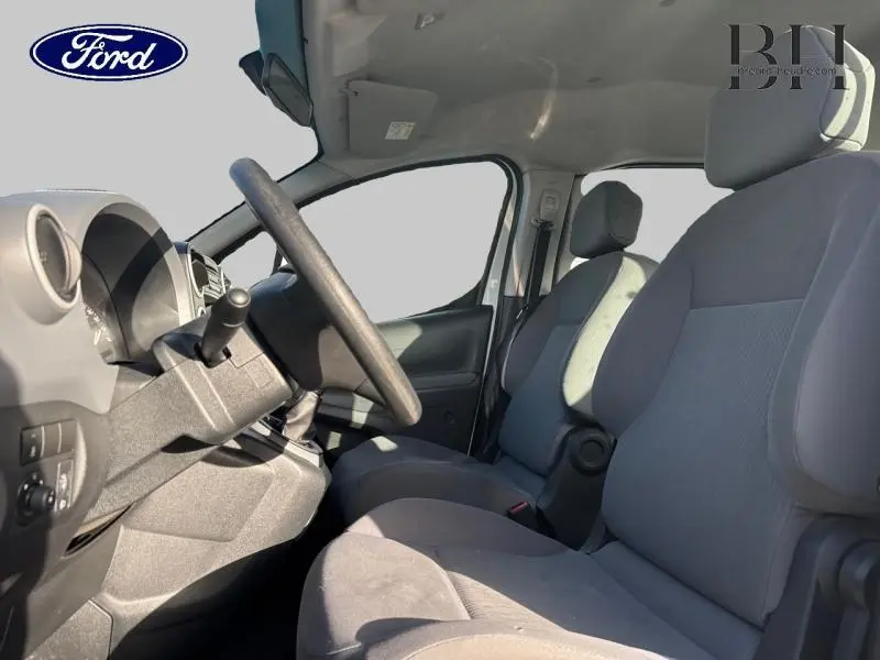 Vue intérieure côté conducteur du Peugeot Partner Tepee blanc Banquise, montrant les sièges en tissu et le volant réglable.