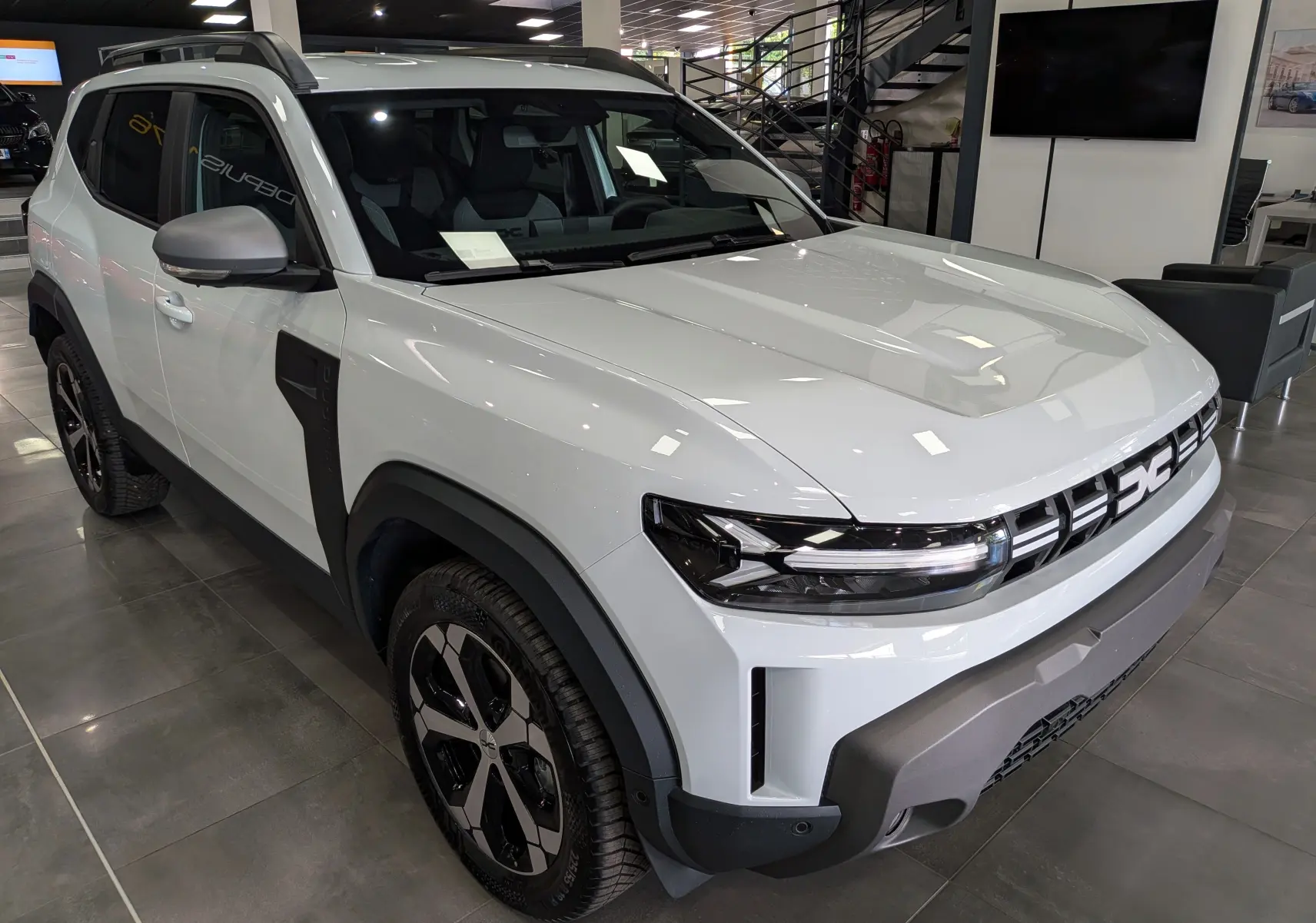 SUV Dacia Duster Hybrid-G blanc Glacier vu en 3/4 avant droit, avec jantes noires et détails noirs contrastants.