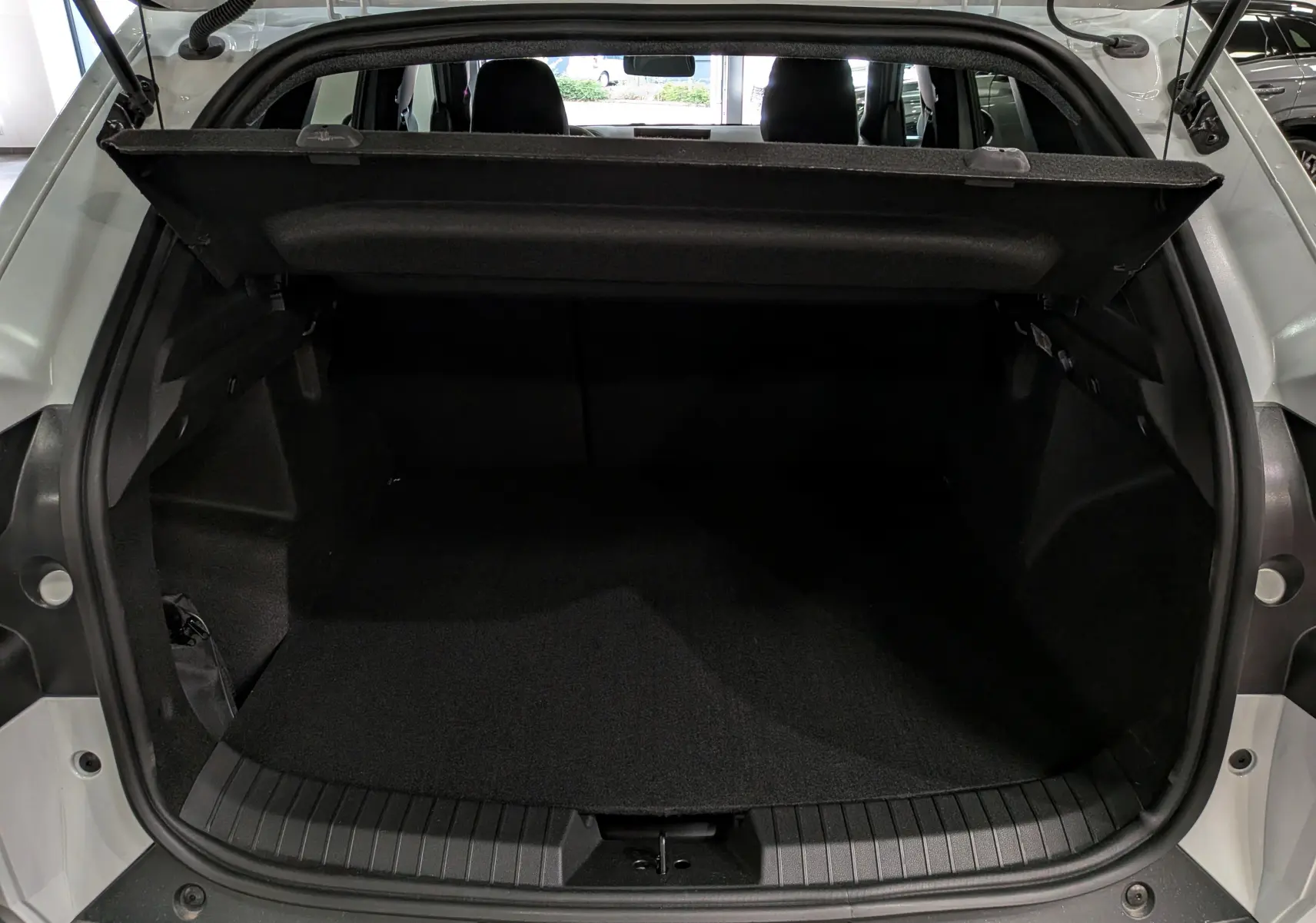 Coffre ouvert vu de l'arrière d'un Dacia Duster Hybrid-G blanc Glacier, montrant l'espace de chargement et la tablette arrière.