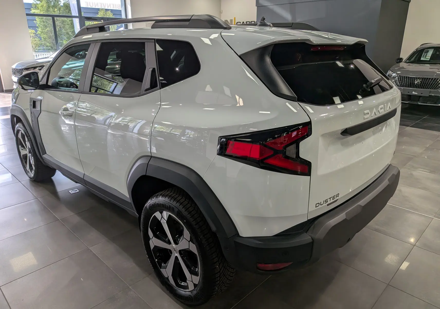 Vue 3/4 arrière droite du Dacia Duster Hybrid-G blanc Glacier, avec jantes biton et éléments noirs contrastants.