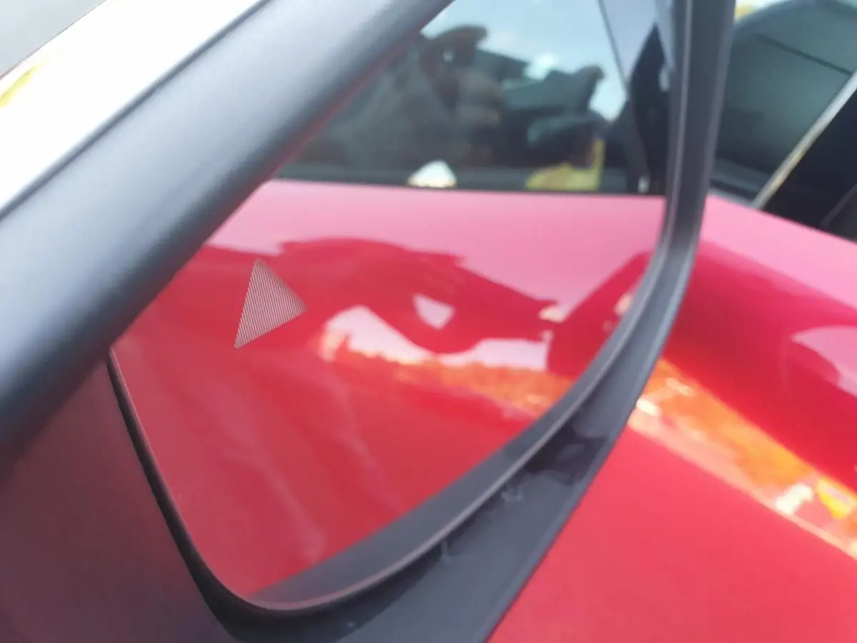 Détail du triangle d'alerte d'angle mort sur la porte côté gauche d'une Renault Clio VI rouge absolu.