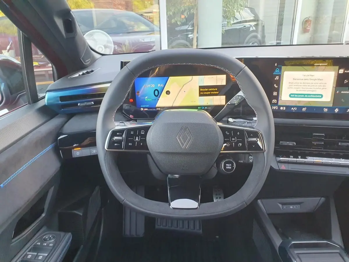Vue frontale du tableau de bord de la Renault Clio VI hybride avec volant compact et écran numérique large.