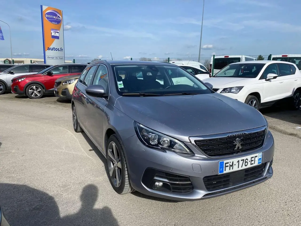 Peugeot 308 SW gris Artense métal vue 3/4 avant droit sur parking avec calandre noire et phares LED.
