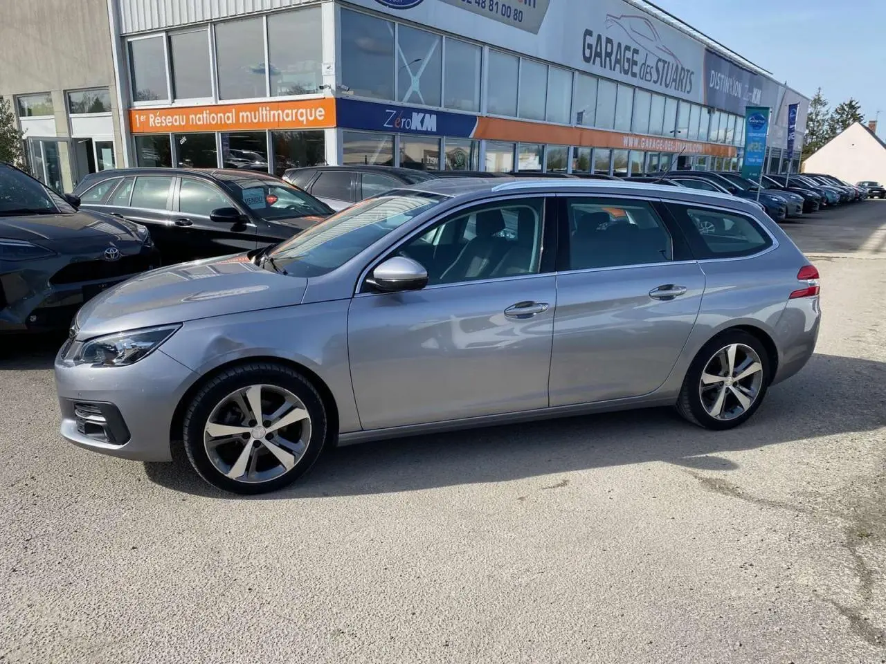 Peugeot 308 SW gris Artense métallisé vue de profil côté gauche, avec barres de toit et jantes alliage.