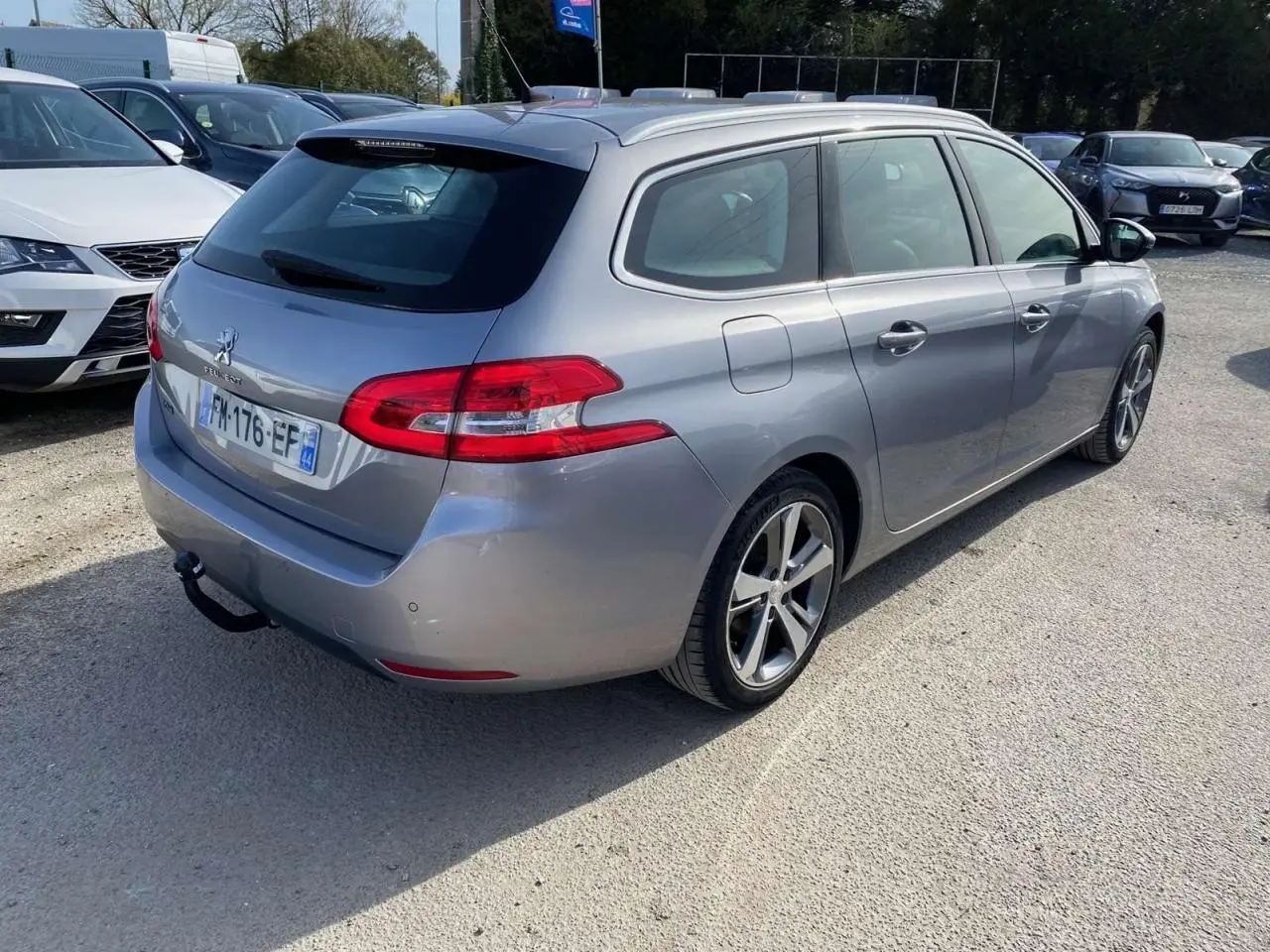 Peugeot 308 SW gris Artense métal vue 3/4 arrière droit avec attelage et barres de toit en aluminium
