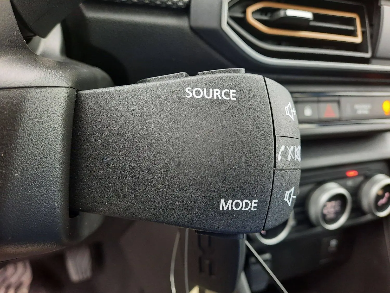 Gros plan sur la commande audio au volant du Dacia Sandero Stepway 2025 noir nacré, avec tableau de bord flou en arrière-plan.