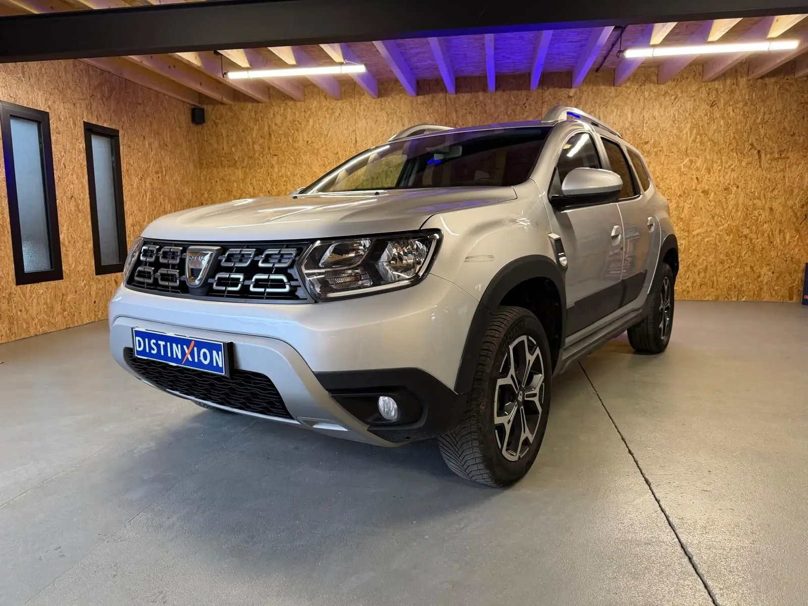 Dacia Duster gris vue 3/4 avant droit en intérieur, avec calandre noire et jantes alliage 17 pouces Maldives.