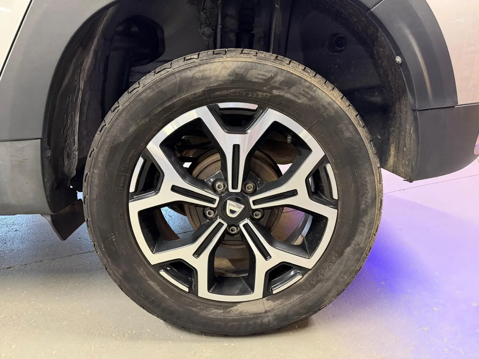 Gros plan sur la roue avant droite du Dacia Duster gris, jante alliage 17'' au design bicolore noir et argent.