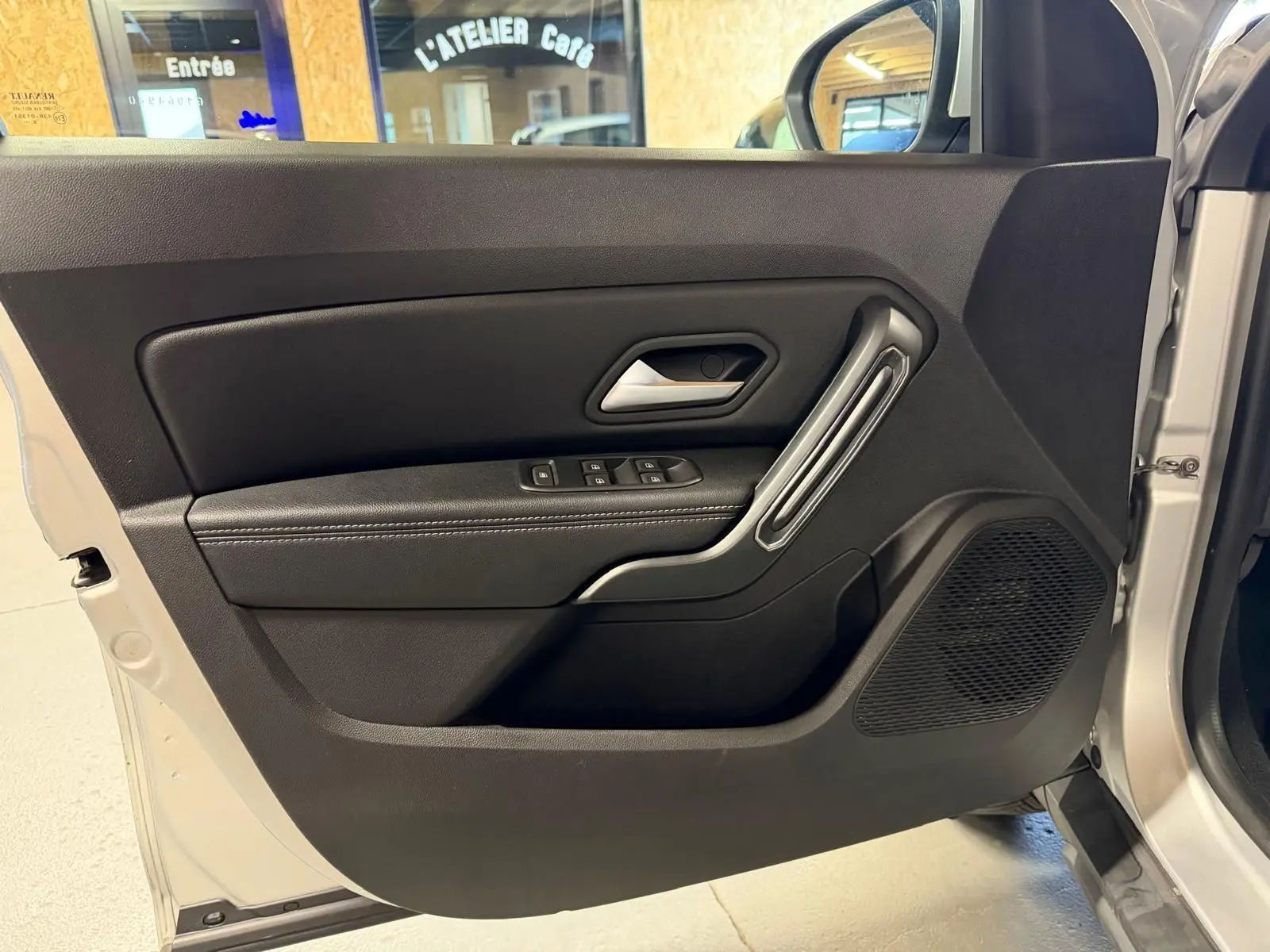 Porte avant gauche ouverte d'un Dacia Duster gris 2019, avec commandes de vitres et poignée argentée intégrée.