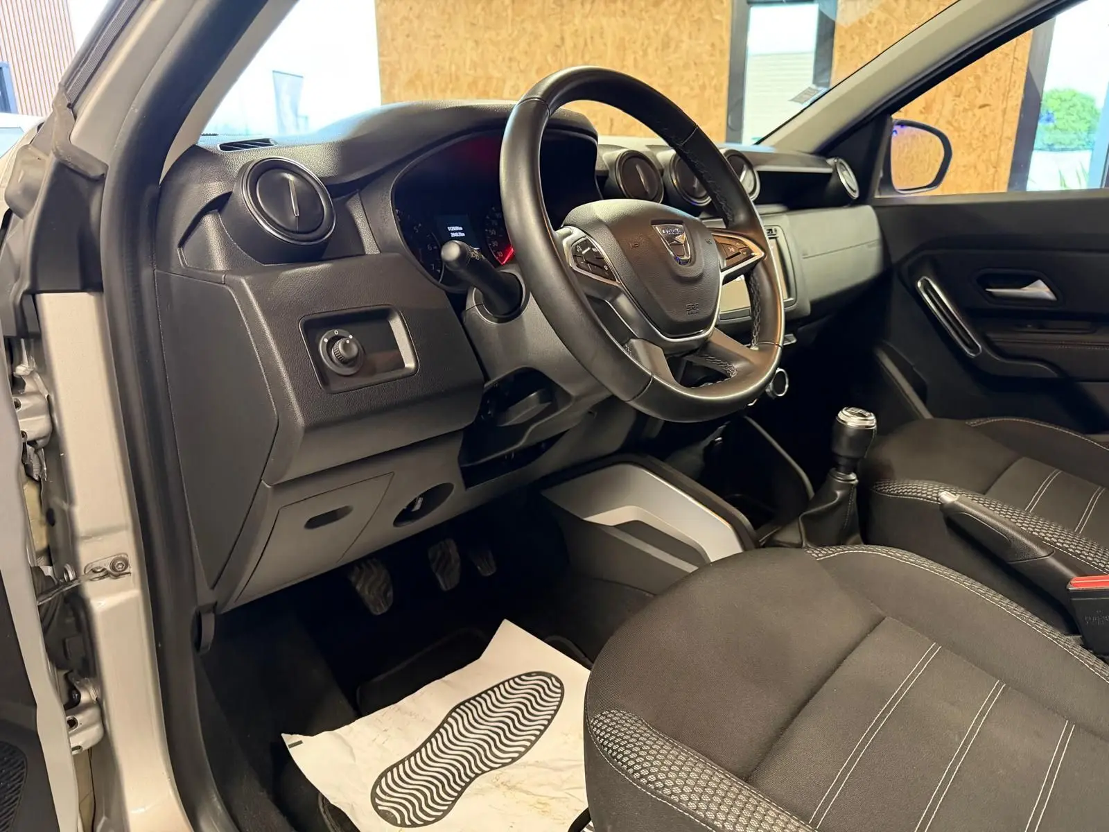 Intérieur côté conducteur du Dacia Duster gris 2019, volant, levier de vitesse et sièges tissu Prestige visibles.