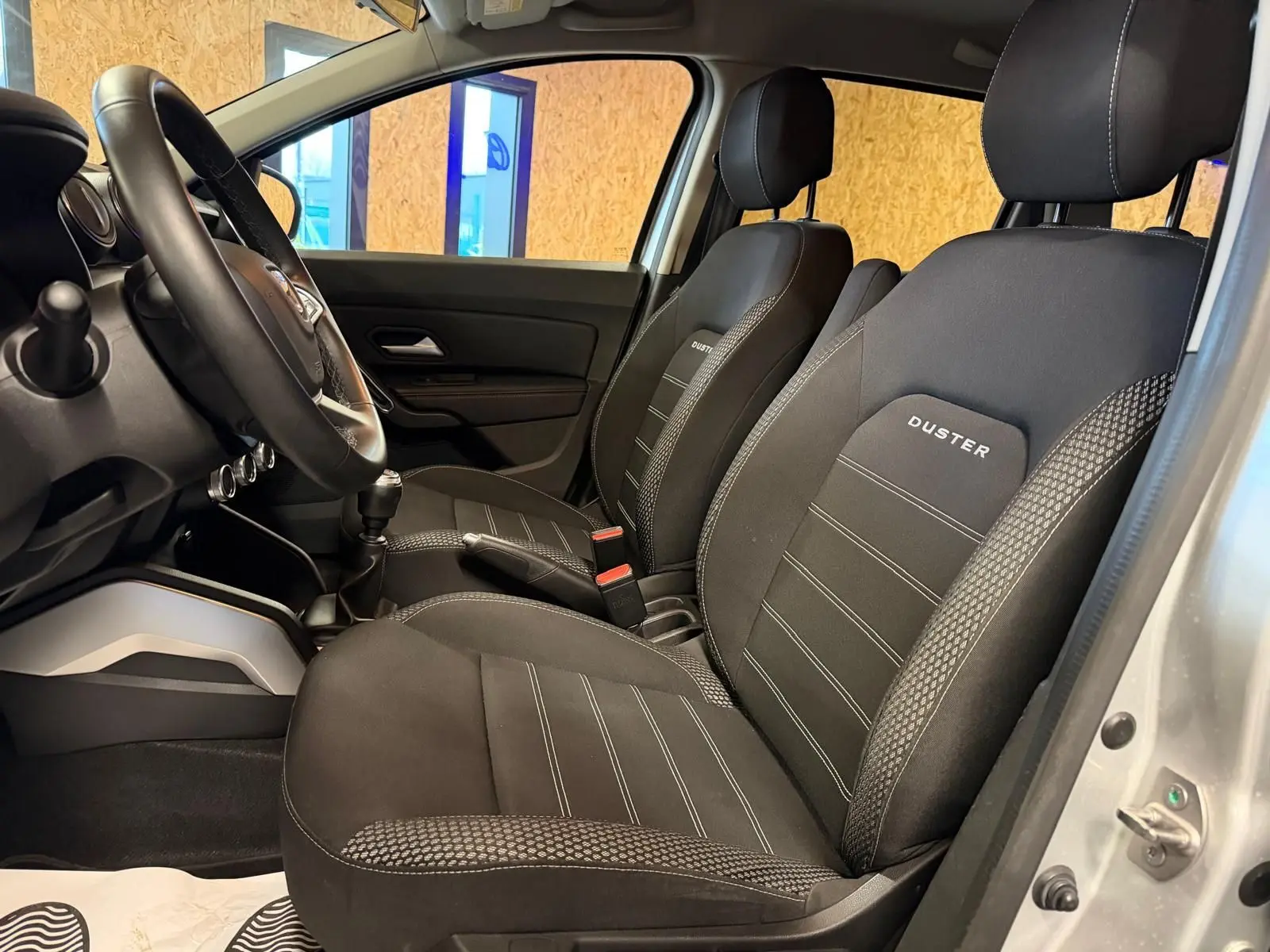 Intérieur côté conducteur du Dacia Duster gris 2019, sièges tissu noir avec logo DUSTER brodé sur appuie-têtes.