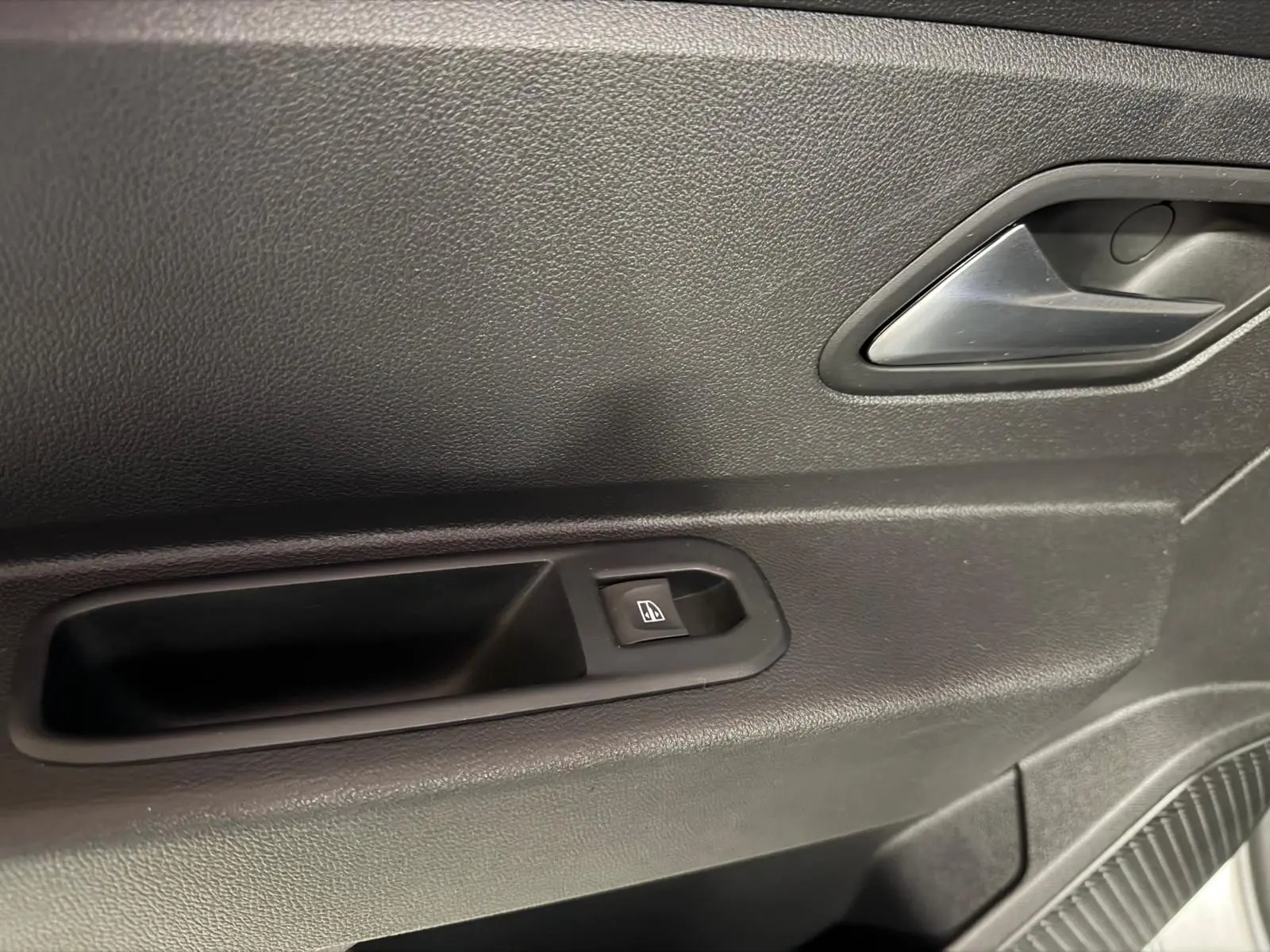 Gros plan sur la poignée intérieure et le bouton de lève-vitre côté gauche d'une porte de Dacia Duster gris.