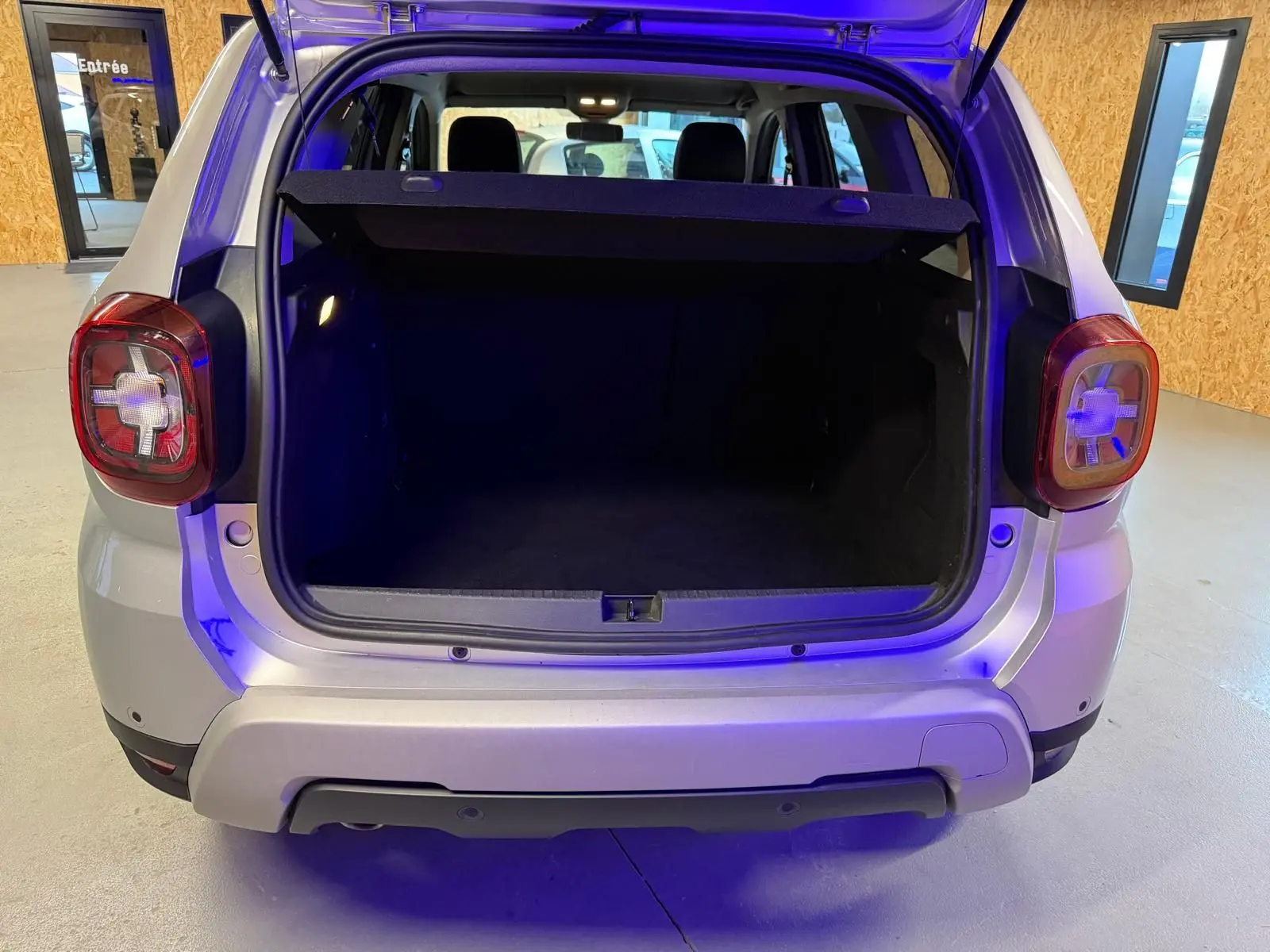 Coffre ouvert vu de l'arrière d'un Dacia Duster gris 2019 avec hayon et feux arrière caractéristiques visibles.