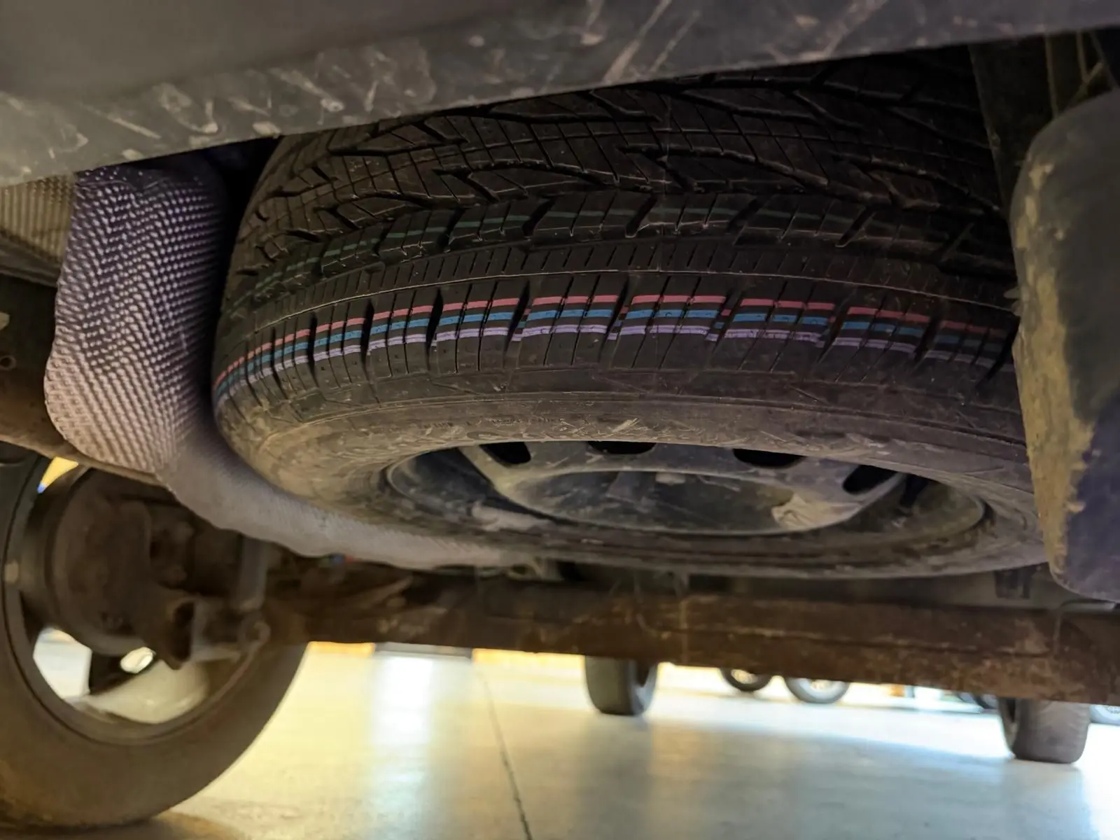 Vue sous le Dacia Duster gris 2019 montrant la roue de secours montée sur jante acier sous le châssis arrière.