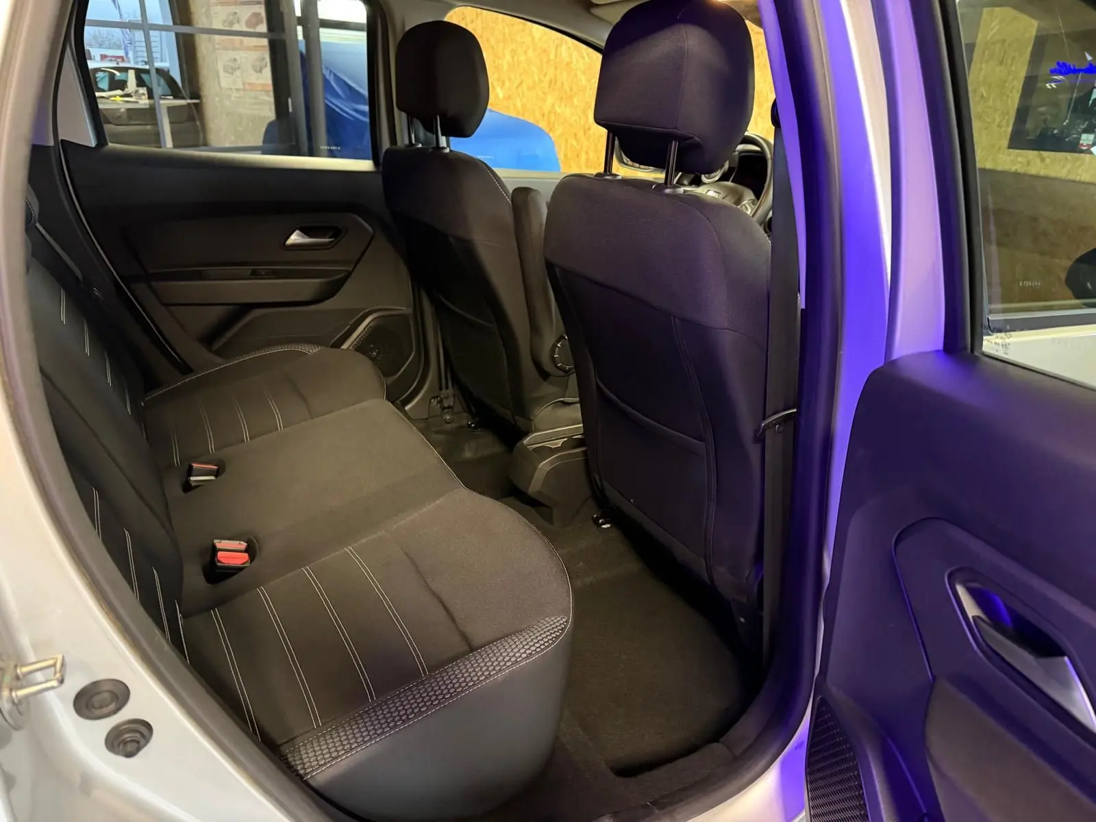 Vue intérieure côté droit sur la banquette arrière noire du Dacia Duster gris, avec portes ouvertes et sièges avant visibles.