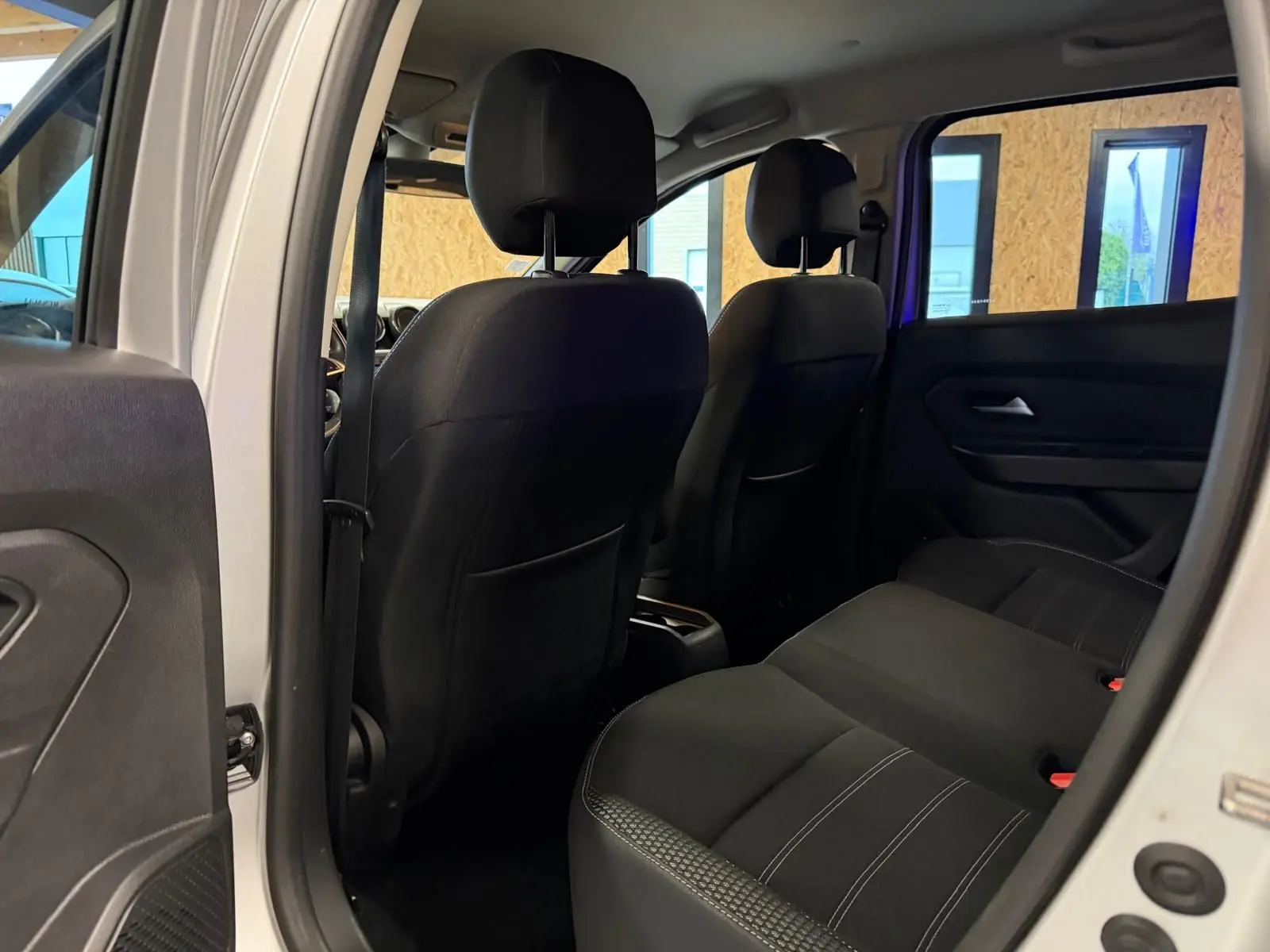 Vue intérieure arrière du Dacia Duster 2019 avec sièges tissu noir et surpiqûres blanches visibles côté droit.