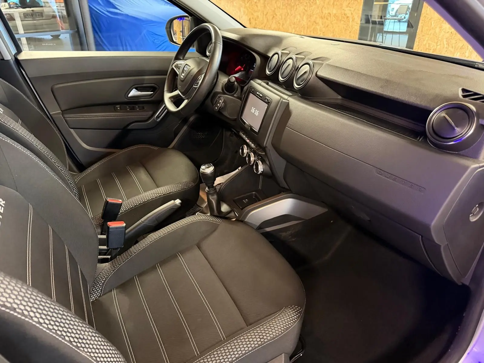 Intérieur avant droit du Dacia Duster 2019 avec sellerie tissu noire, tableau de bord épuré et volant multifonction.