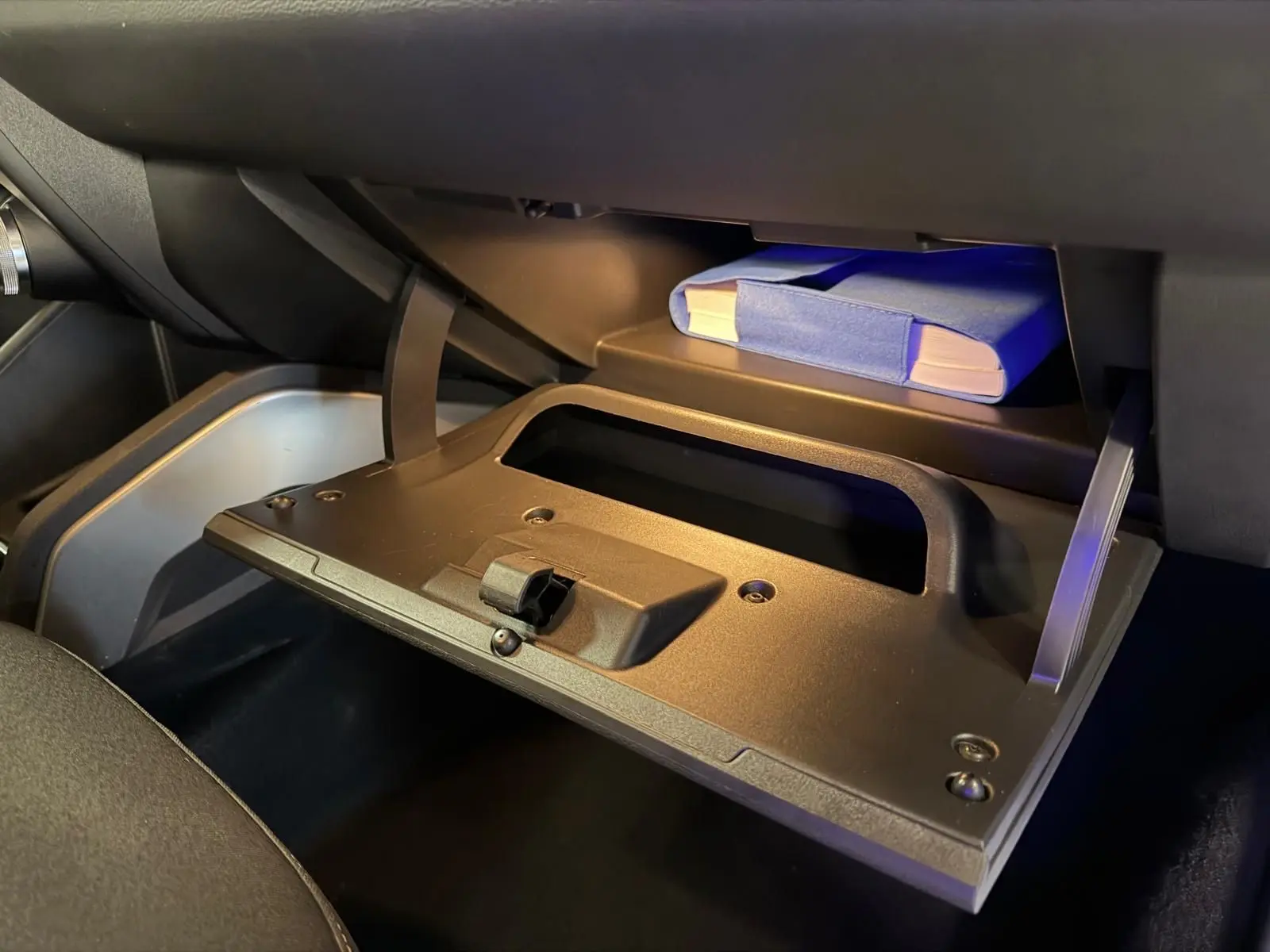 Gros plan sur la boîte à gants ouverte du Dacia Duster gris 2019, avec un manuel bleu visible à l'intérieur.