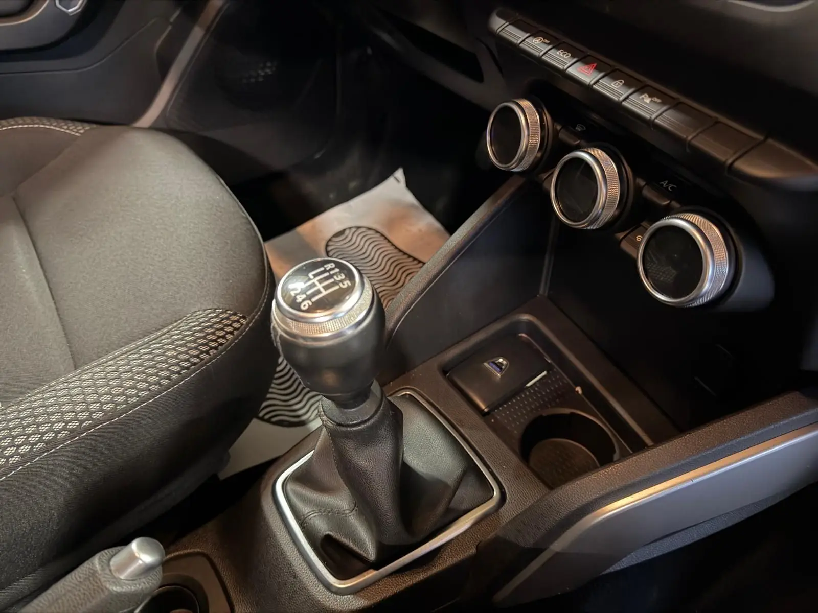 Gros plan sur la commande de boîte manuelle et la console centrale du Dacia Duster gris, avec commandes de climatisation rondes.