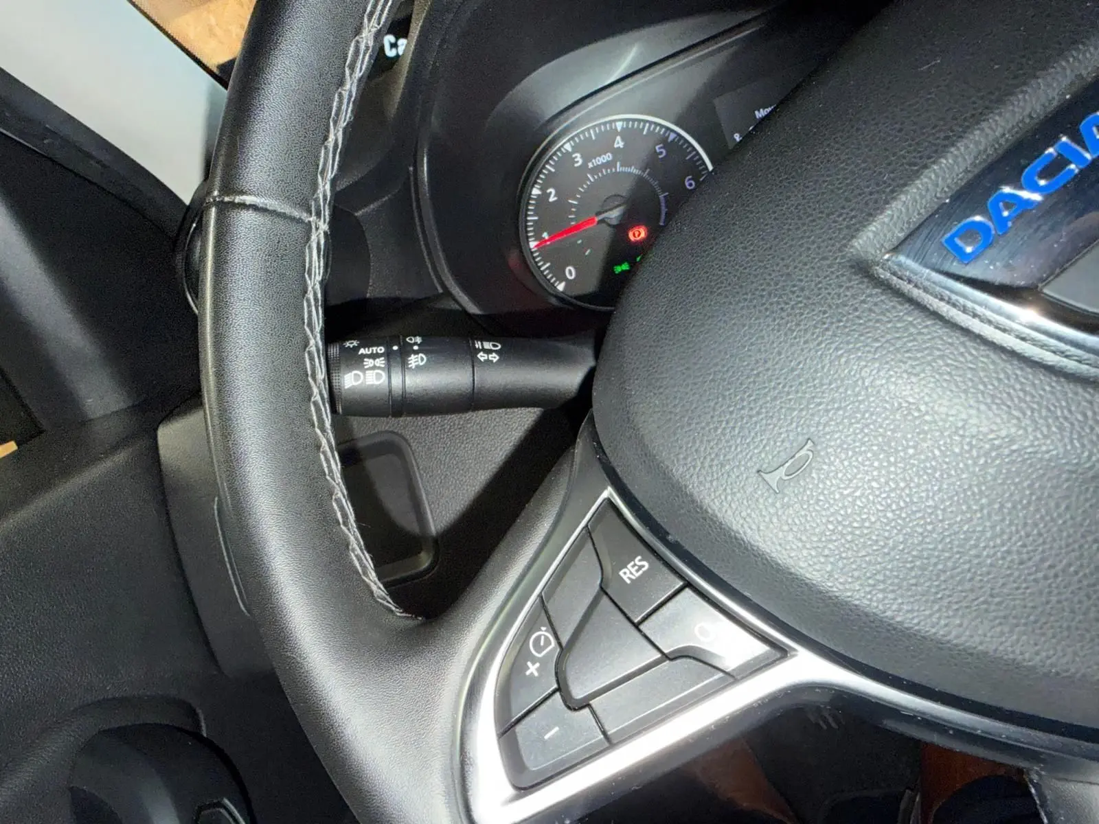 Gros plan sur le volant noir avec commandes intégrées du Dacia Duster gris 2019, tableau de bord en arrière-plan.