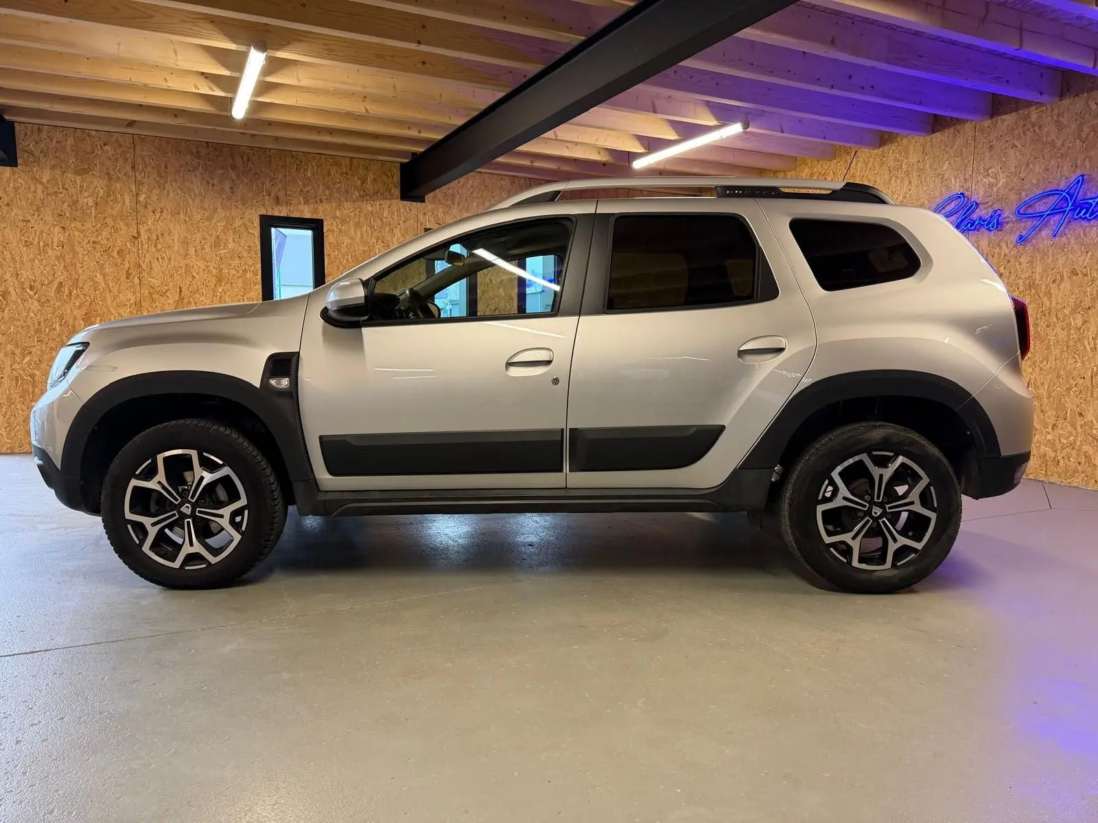 Profil côté gauche du Dacia Duster gris 2019 avec jantes alliage 17'' Maldives et protections noires sur les portes.