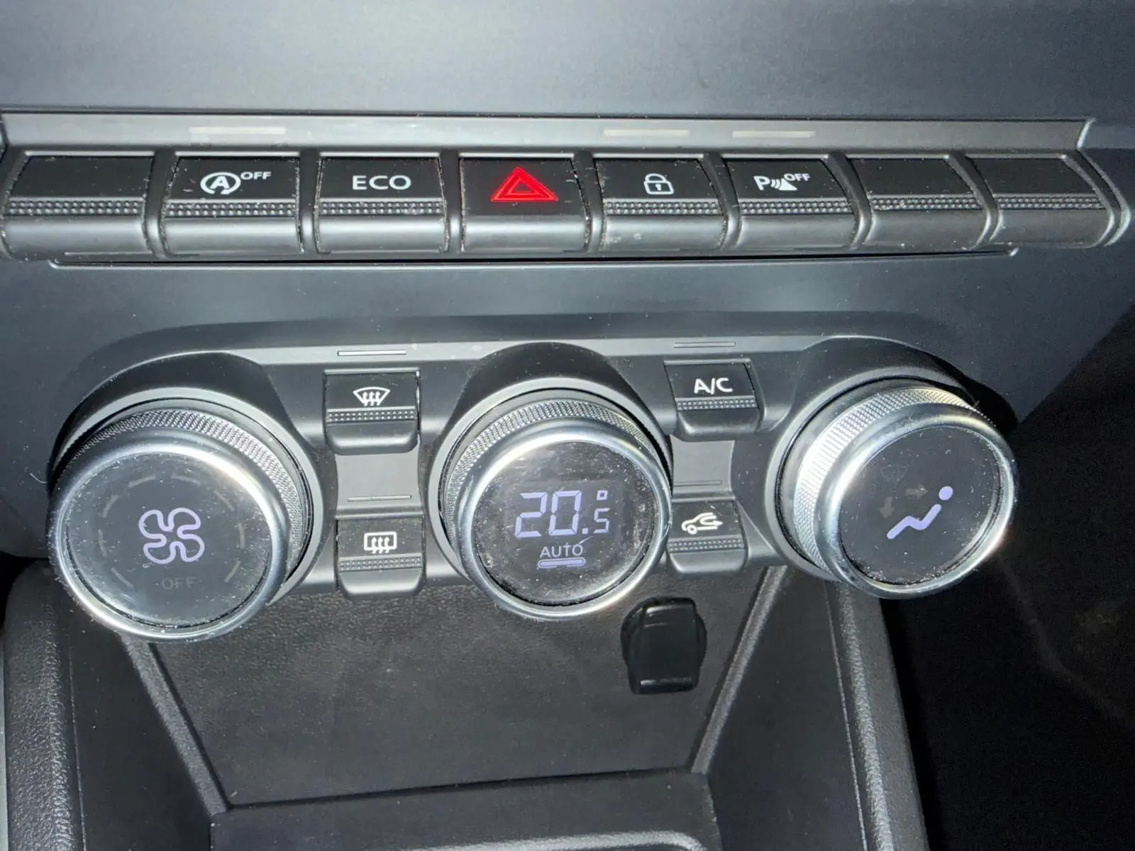 Gros plan sur les commandes de climatisation automatique du Dacia Duster gris, avec affichage digital à 20,5°C.