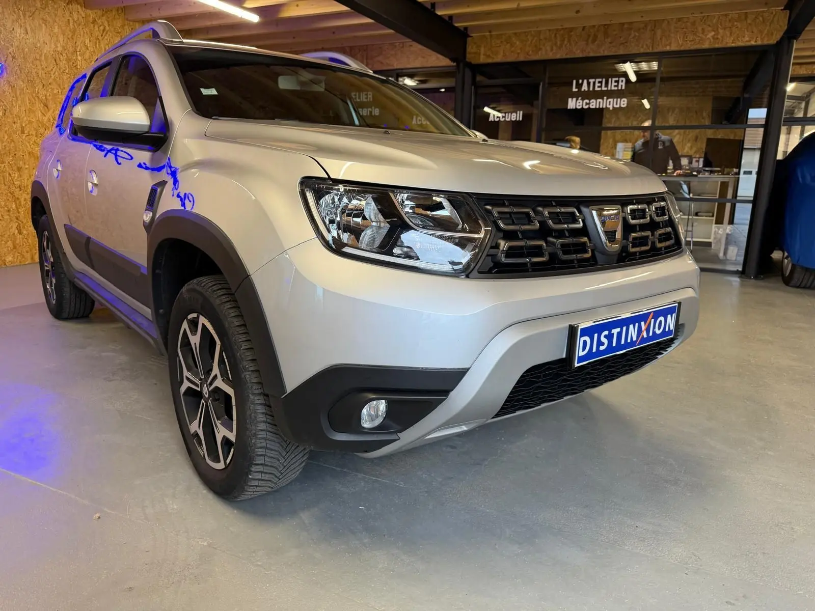 Dacia Duster gris vue 3/4 avant droit, avec calandre noire et jantes alliage 17 pouces Maldives visibles.