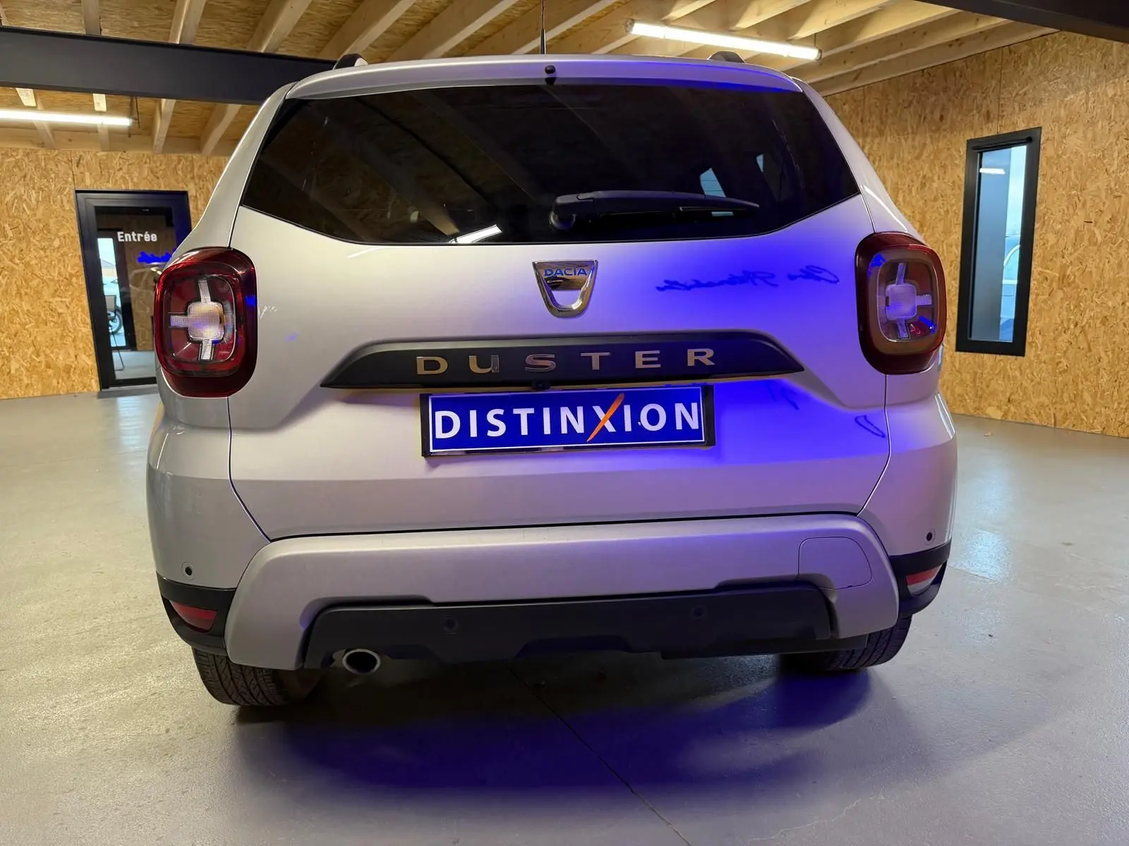 Vue arrière d'un Dacia Duster gris 2019 avec feux arrière carrés et plaque Distinxion dans un garage.