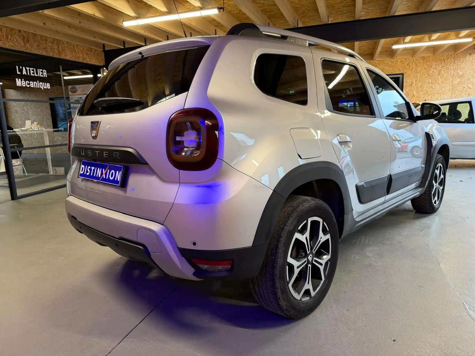 Vue 3/4 arrière droite du Dacia Duster gris 2019 avec jantes alliage et barres de toit en intérieur d'atelier.