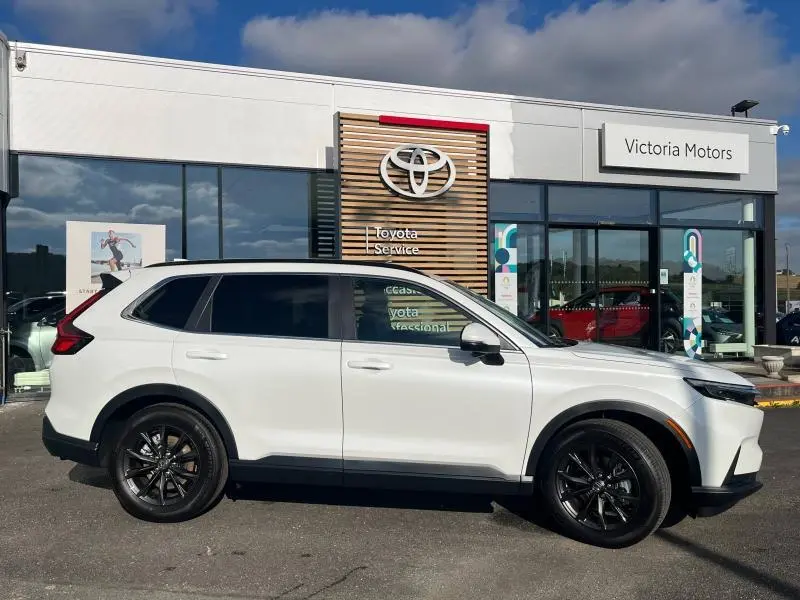 Vue de profil côté gauche d'un Honda CR-V 2024 blanc Diamant Brillant Premium métallisé avec jantes noires devant un concessionnaire.