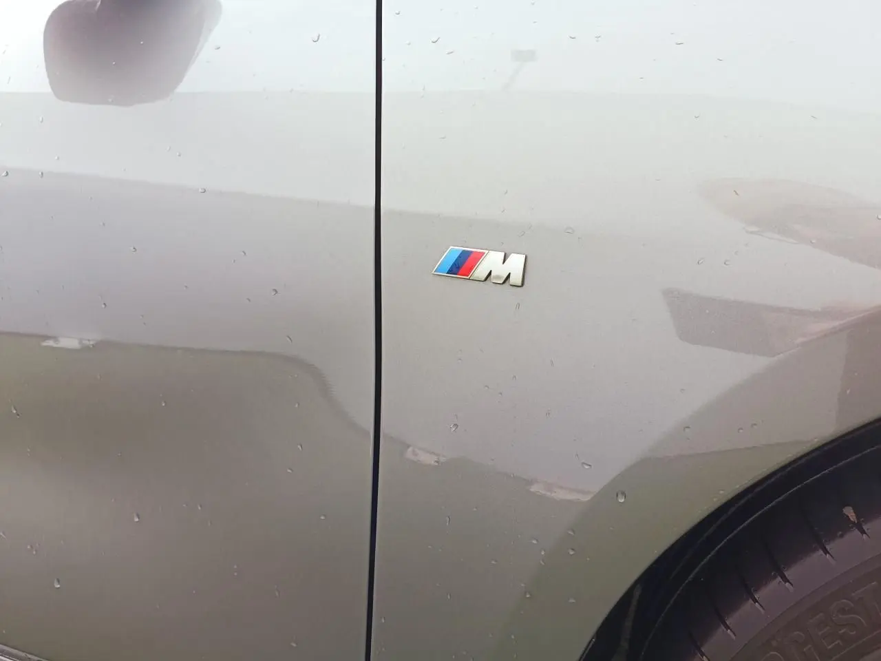 Gros plan sur l'aile avant droite grise Skyscraper d'une BMW Série 1 M Sport avec logo M coloré visible.