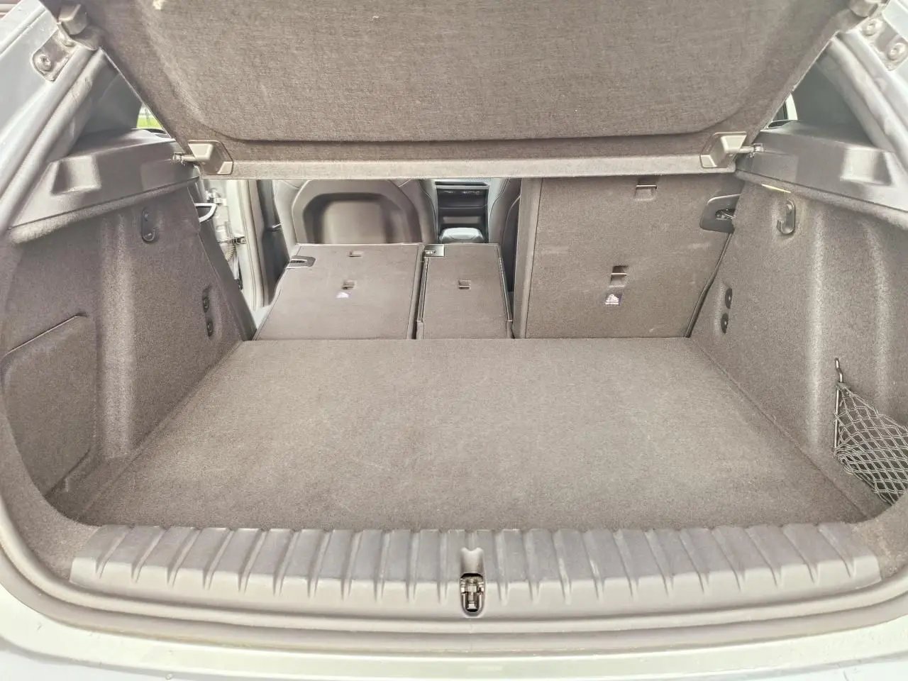 Coffre ouvert de BMW Série 1 gris, banquette arrière rabattue partiellement côté droit, vue depuis l'arrière.