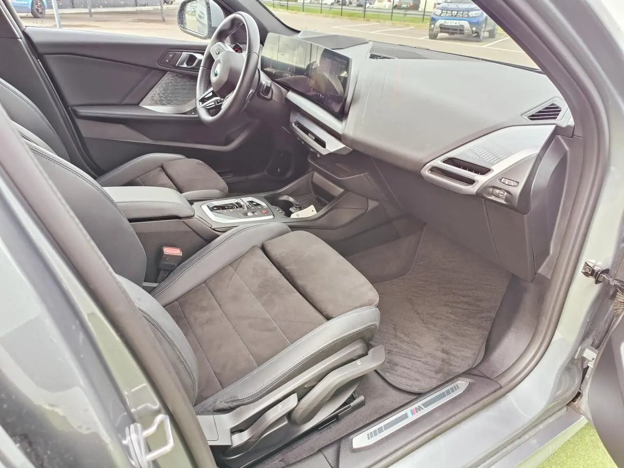 Vue intérieure côté conducteur de la BMW Série 1 M Sport 2025, sièges Alcantara noirs et tableau de bord moderne.