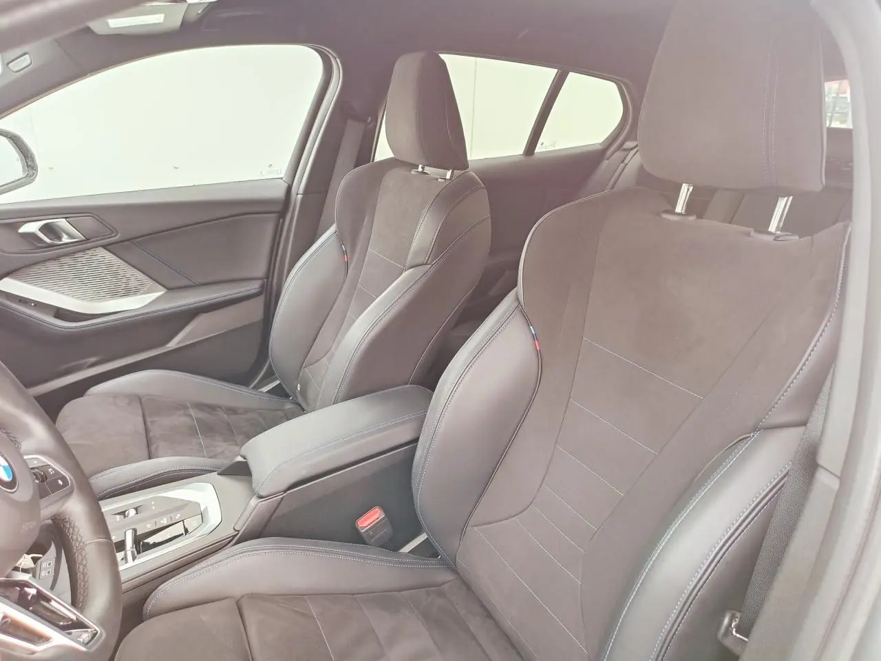 Vue intérieure côté droit sur les sièges sport Alcantara noirs avec surpiqûres bleues et accoudoir central de la BMW Série 1.