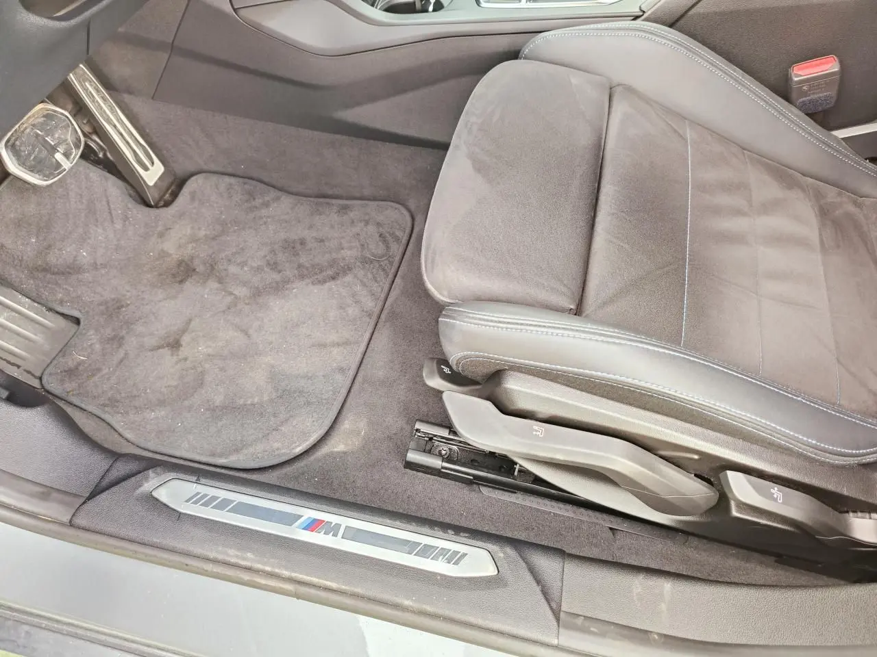 Vue intérieure côté conducteur de la BMW Série 1 M Sport 2025, siège Alcantara noir avec surpiqûres bleues et seuil M.