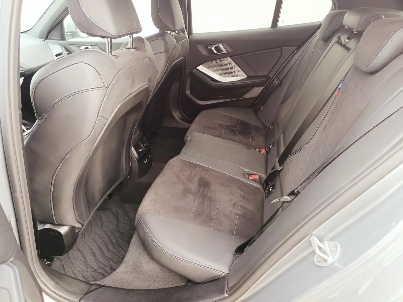 Vue côté droit de la banquette arrière en sellerie Alcantara noire avec surpiqûres bleues dans une BMW Série 1 2025.
