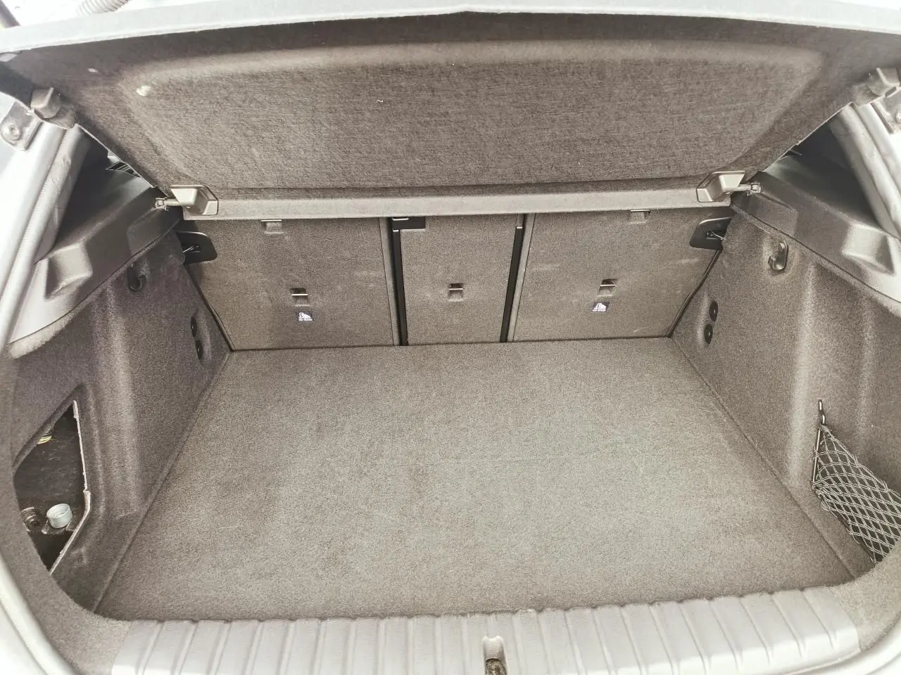 Coffre ouvert de BMW Série 1 F70 gris Skyscraper, vue intérieure montrant la banquette arrière rabattable et filet de rangement côté droit.