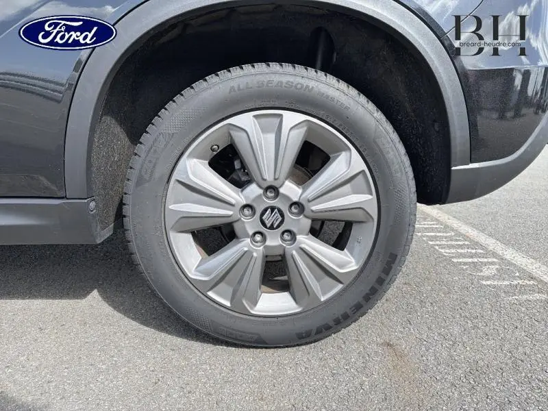 Gros plan sur la roue avant gauche du Suzuki Vitara Cosmic Black Pearl métallisé avec jante alu et logo Suzuki central.